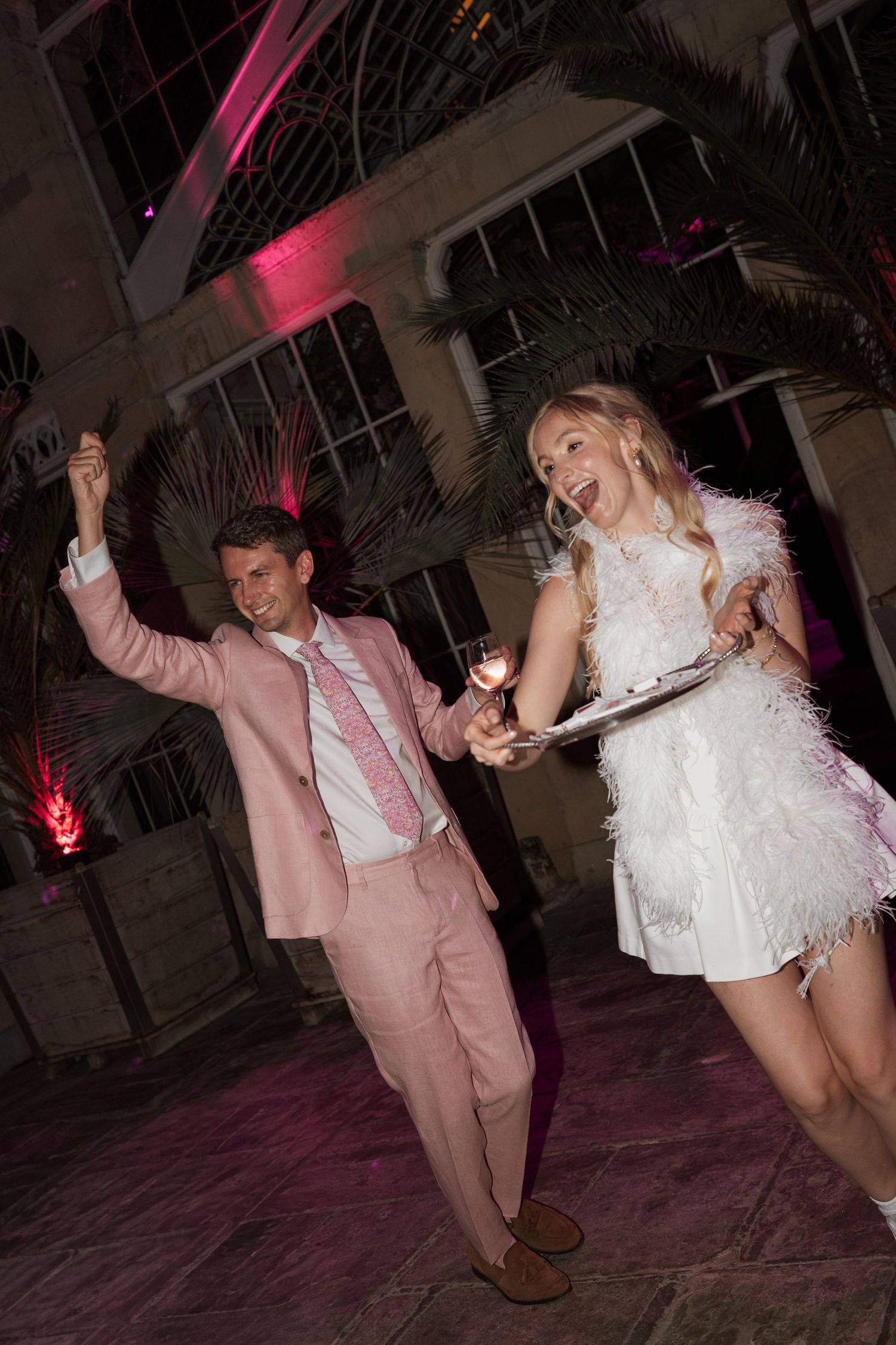 Energetic dancing at a wedding reception with pink lighting effects.