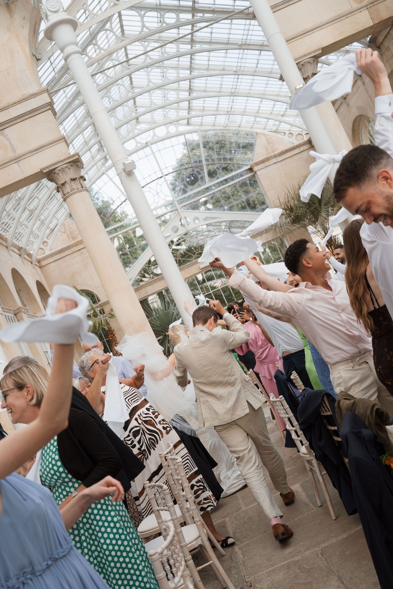 People celebrating in an elegant glass-roofed conservatory with white decor.