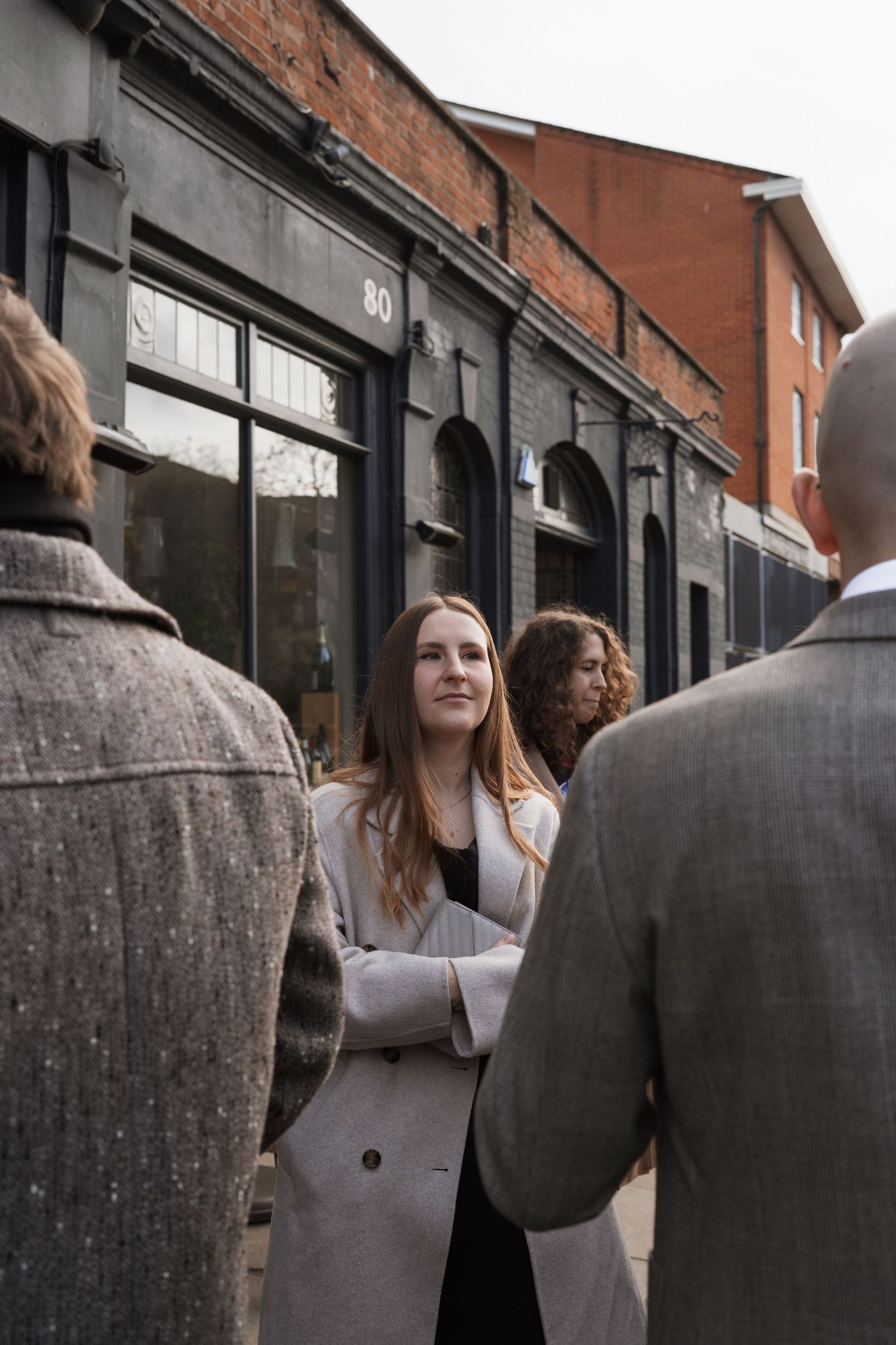 People standing close together outside a brick building on an overcast day.
