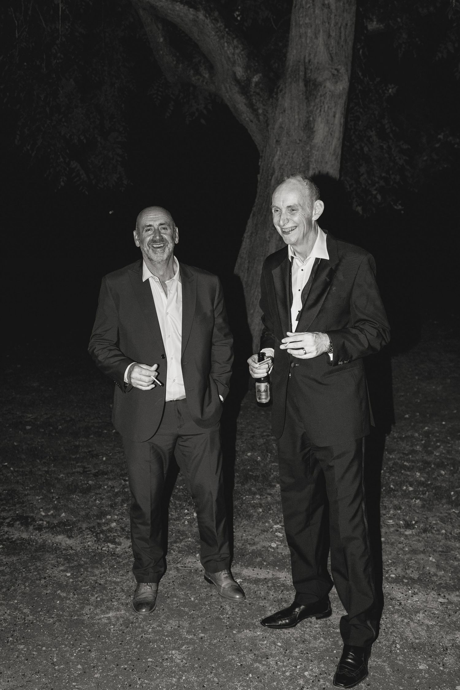 Two people in suits standing and chatting outdoors at night.