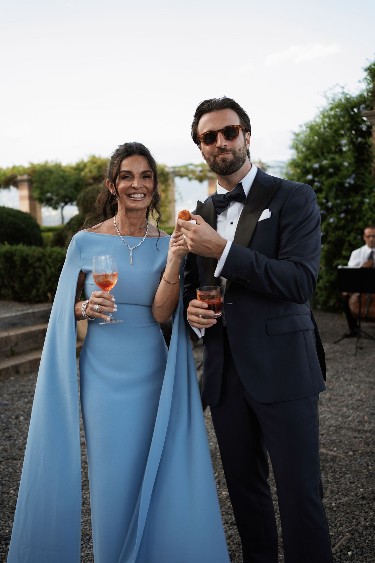 Couple in formal attire holding drinks at an outdoor celebration.