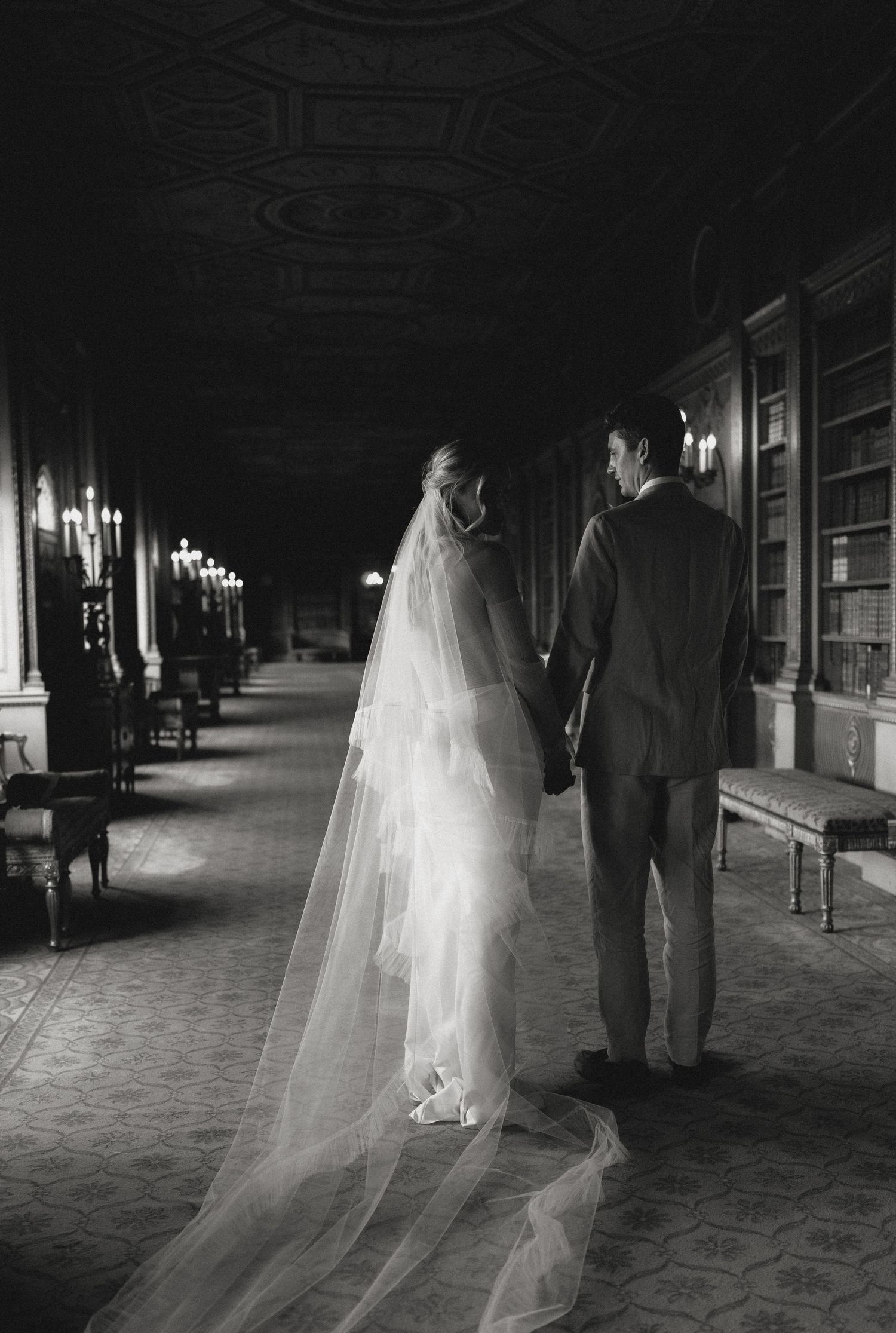 Black and white photo of wedding couple walking through a grand historic corridor.