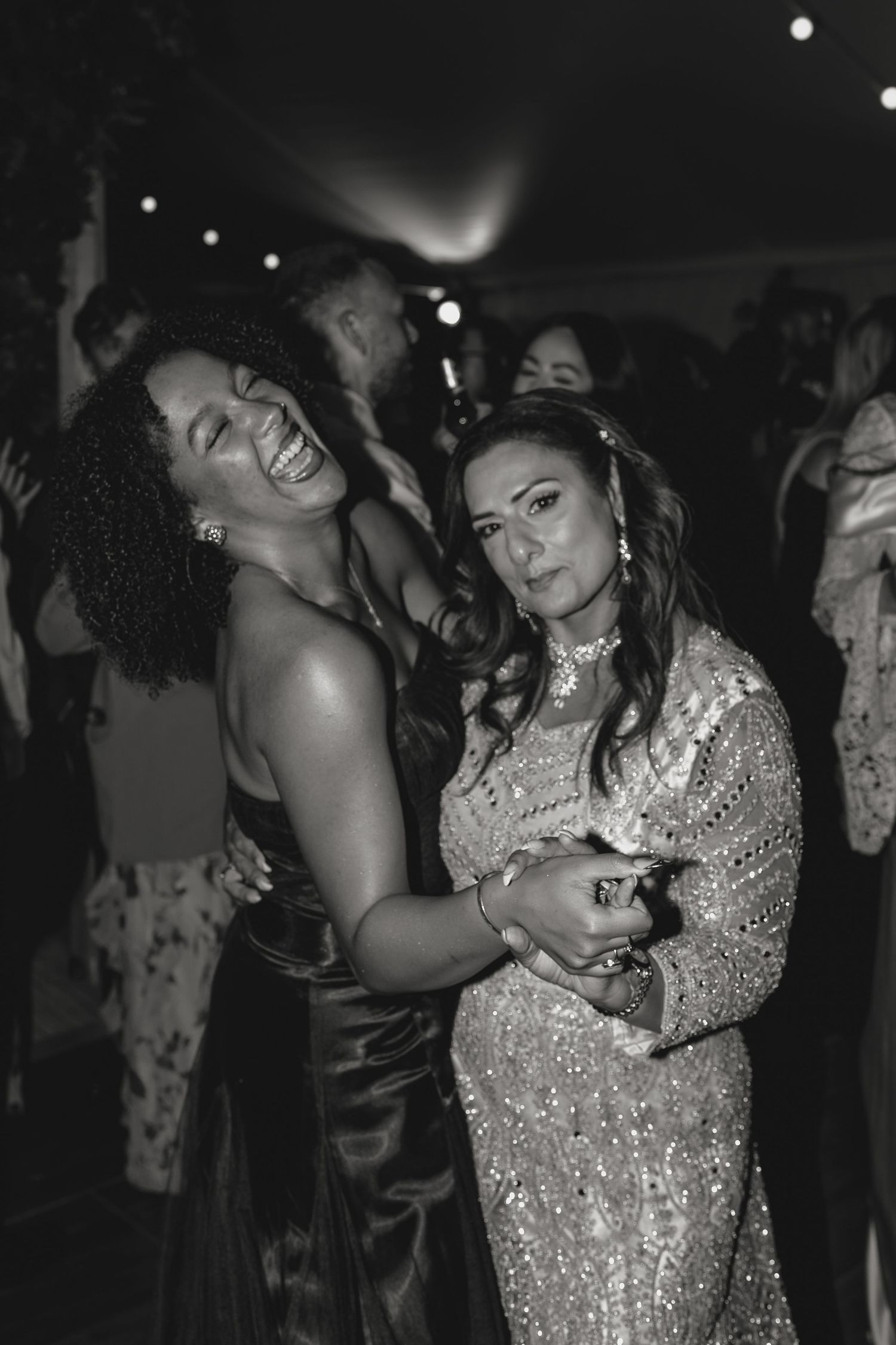 Party guests dance joyfully in sparkling formal attire at a nighttime celebration.
