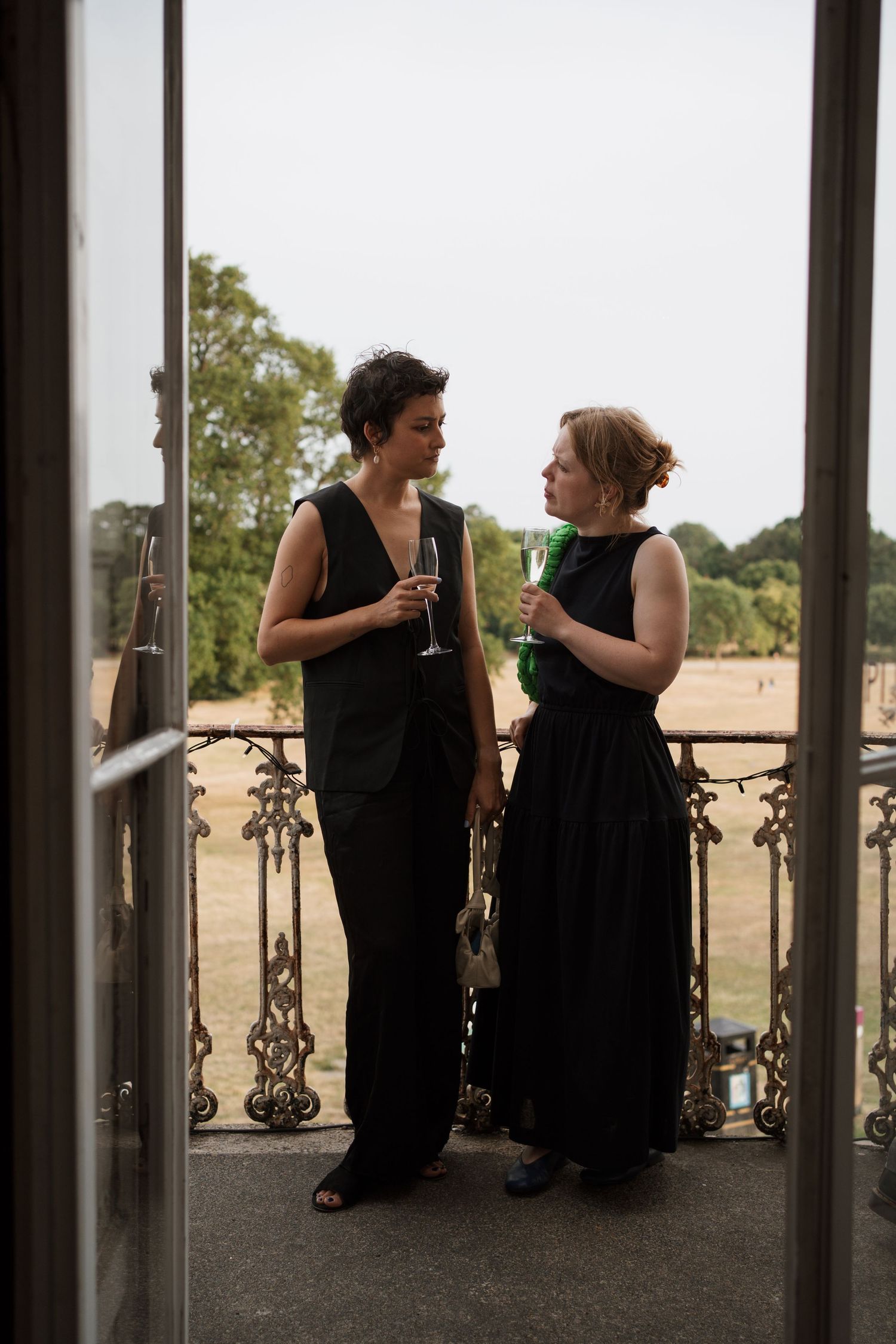 Two people in black dresses having a conversation on an outdoor balcony at sunset.