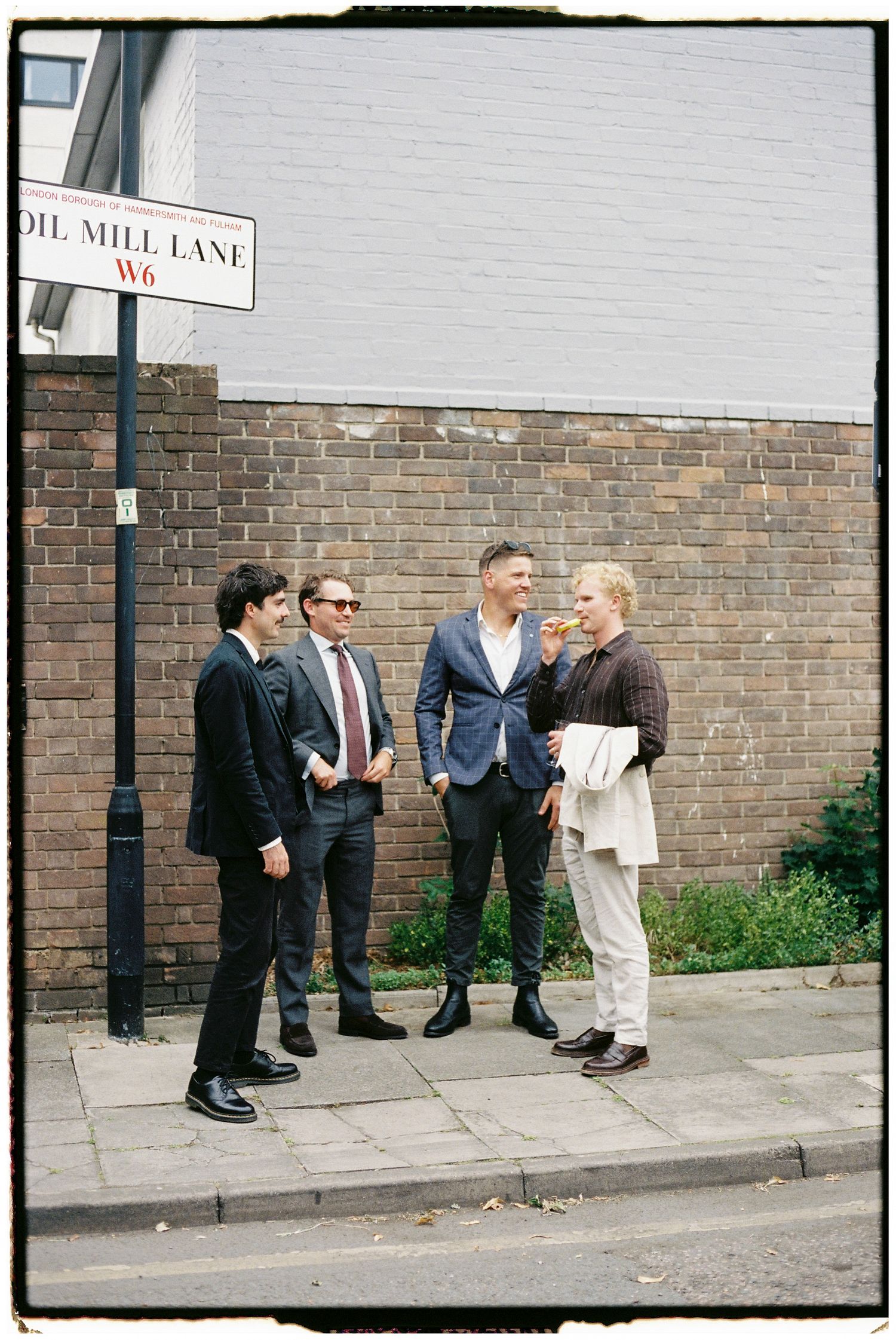 Wedding party gathered outside a brick wall near a street sign.