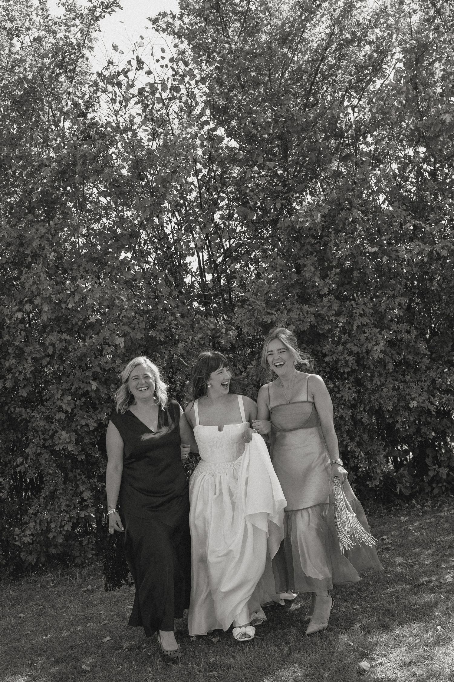 Wedding party poses together in casual style against green foliage backdrop.