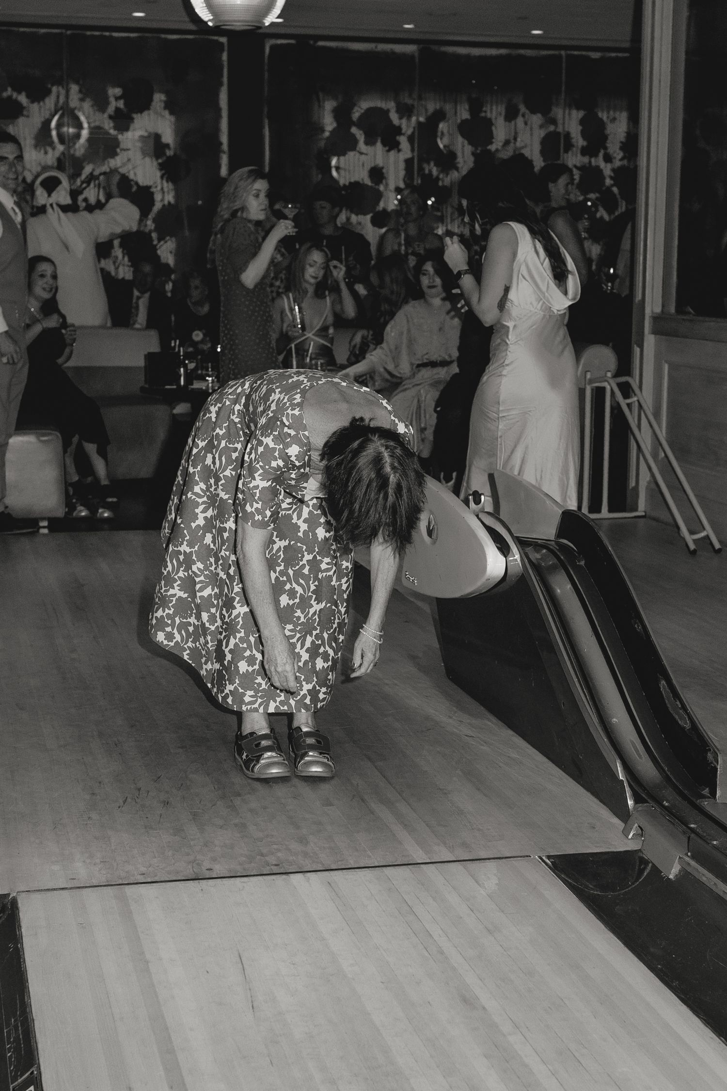 People bowling on multiple lanes in a dimly lit bowling alley.