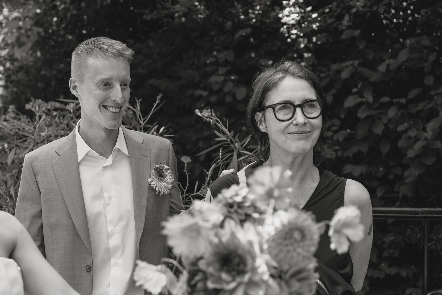 Wedding party members smiling and laughing together in an outdoor garden setting.