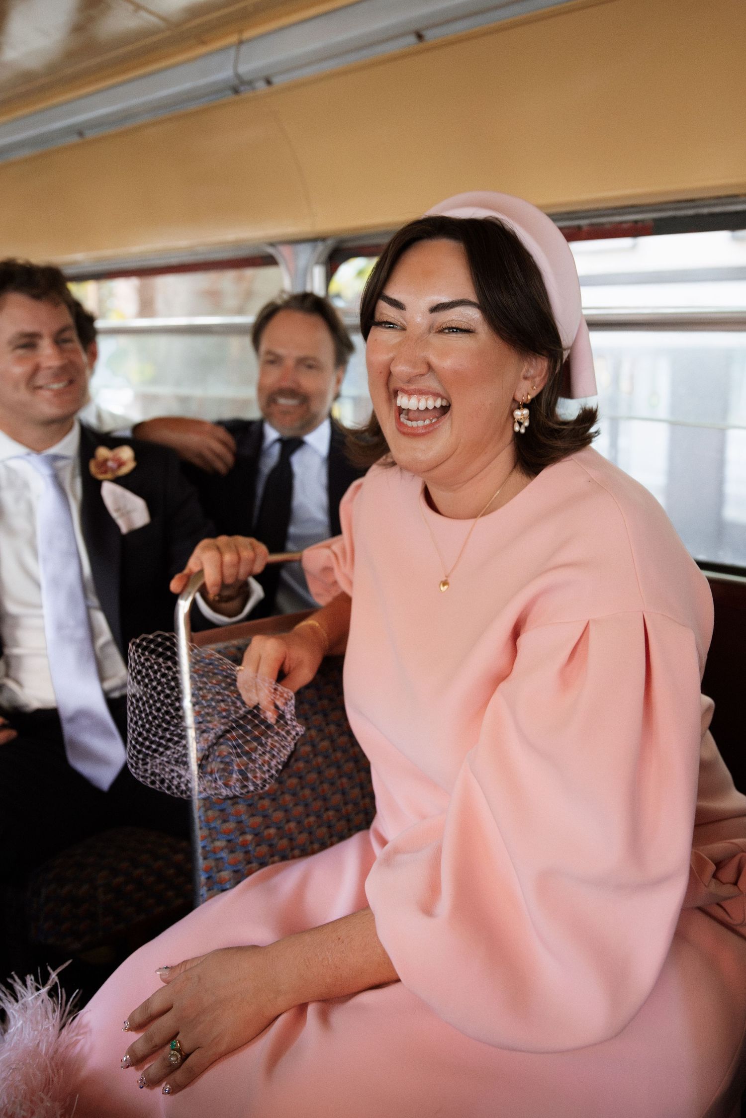 Person wearing a stylish pink statement dress laughs joyfully in what appears to be a vehicle.
