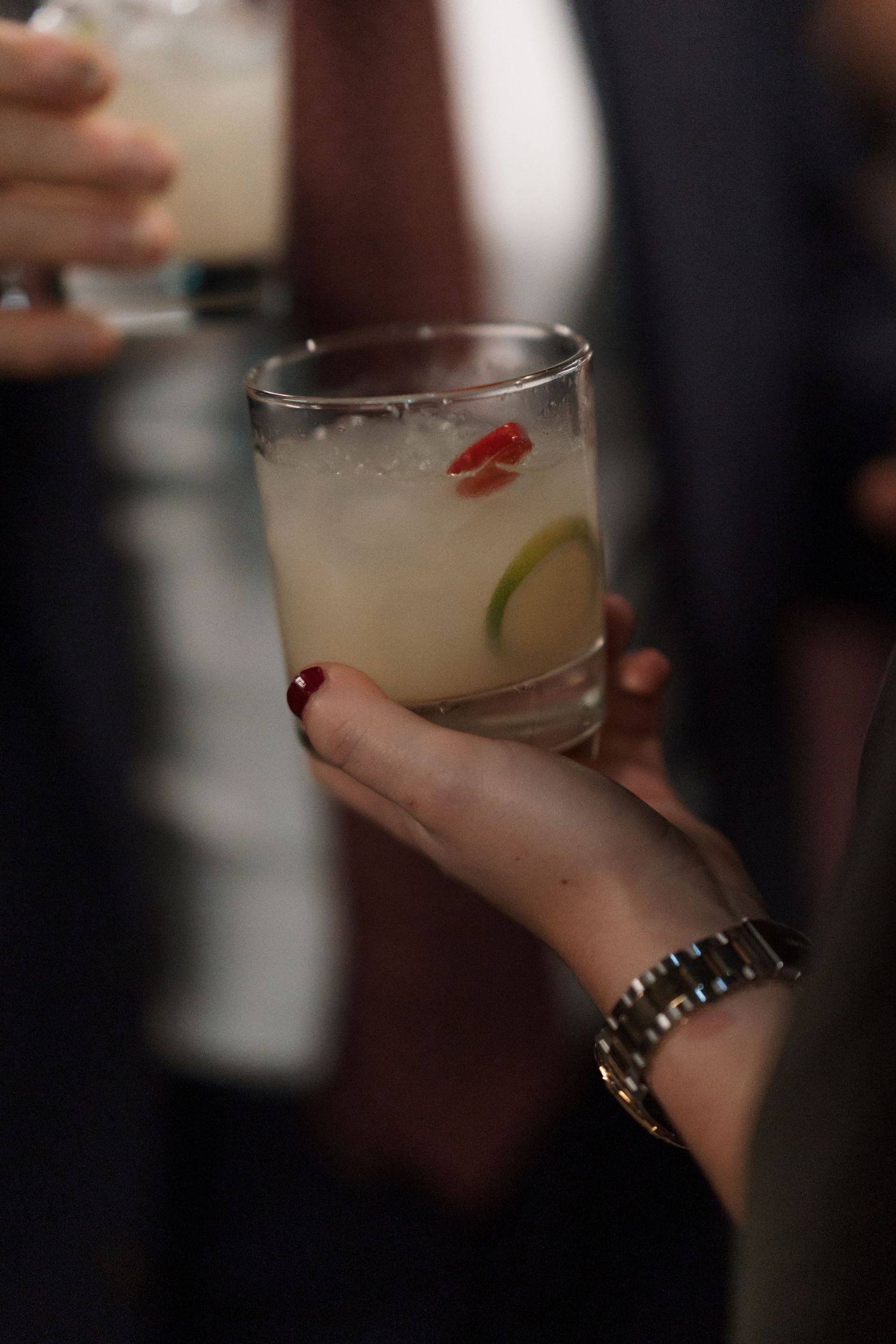 Hand holding a garnished cocktail glass at an evening event.