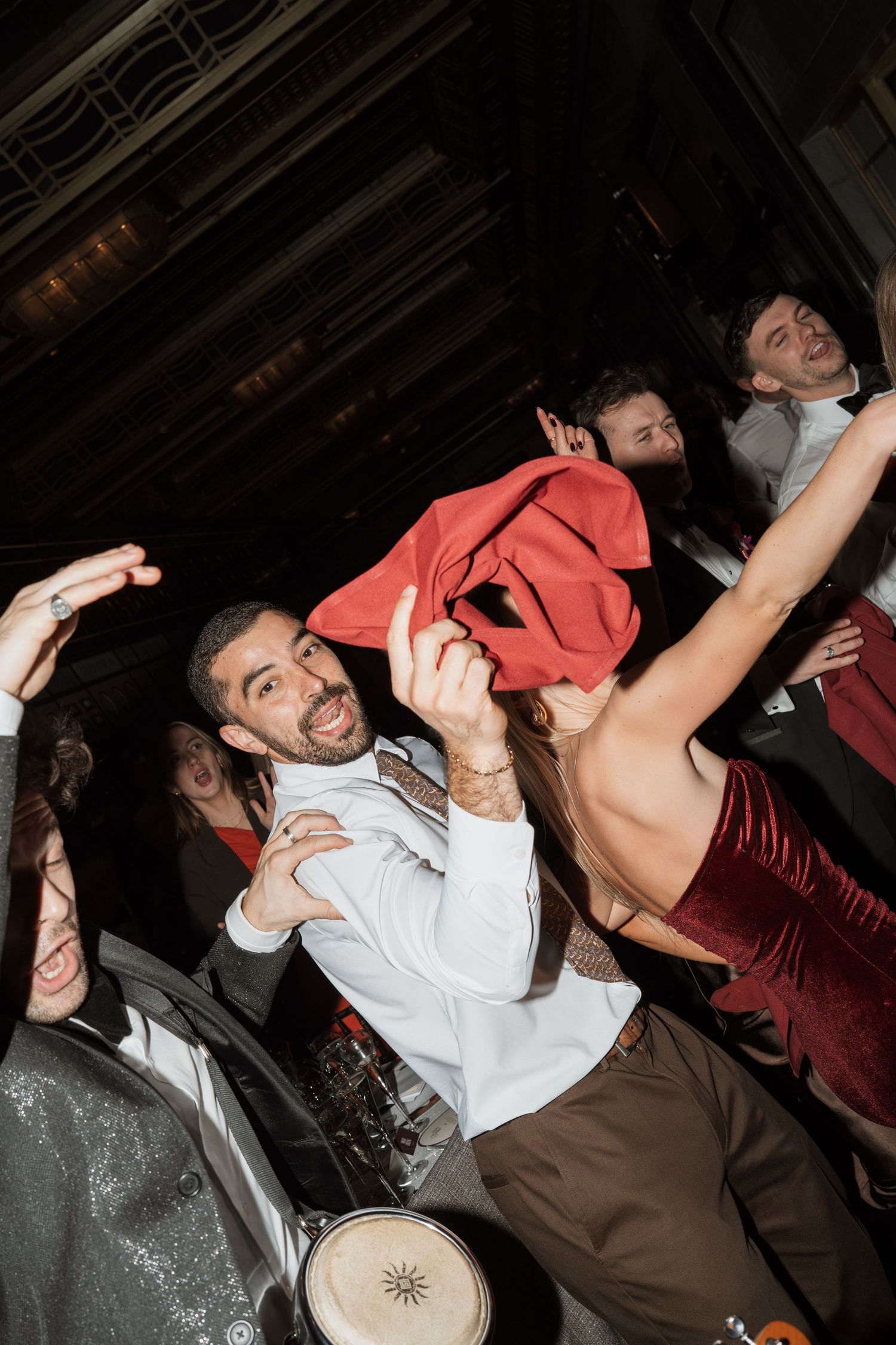 Energetic party crowd dancing and celebrating indoors, with a shirtless person being lifted amid lively guests.
