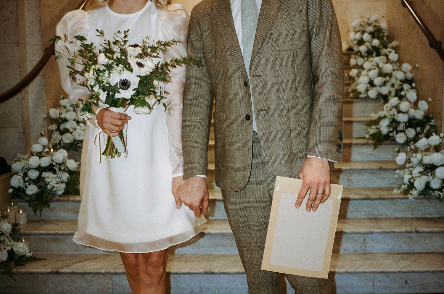 Wedding details showing couple with floral arrangements on marble steps.