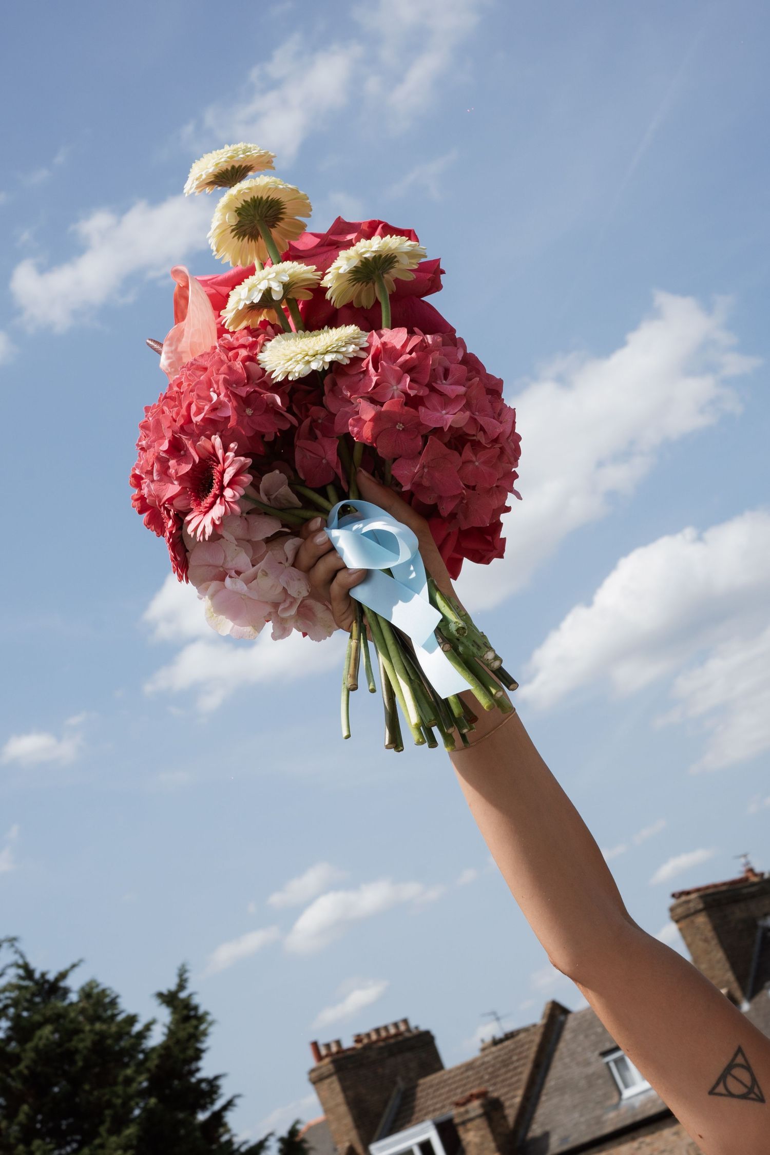 Pink and white wedding bouquet held up against a blue sky.