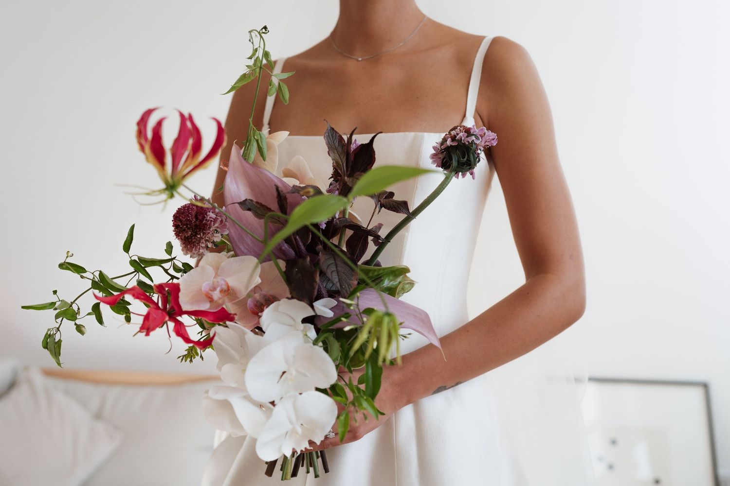 Bride in a white strapless dress holding a lush bouquet of white orchids, pink blooms, red lilies and green foliage.