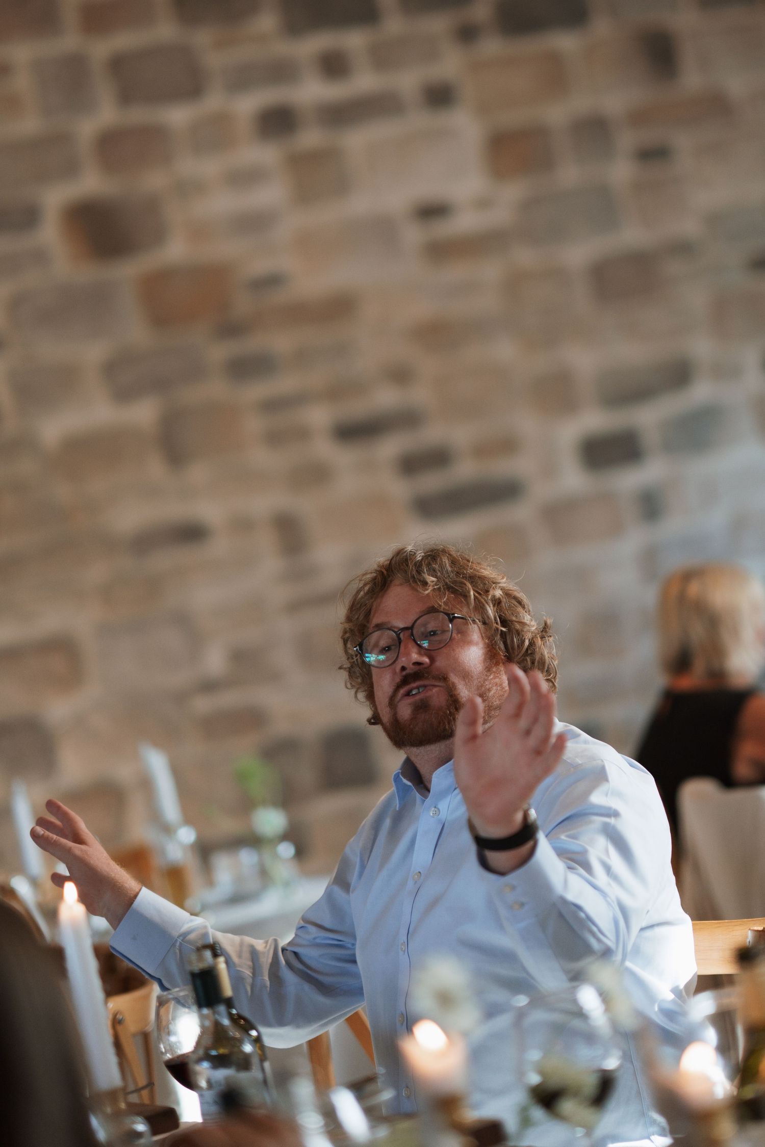 Animated guest enjoying conversation at a wedding reception against a stone wall background.