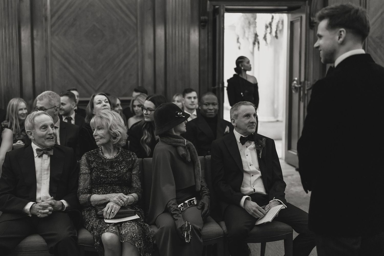 Wedding guests gather in formal attire at an elegant indoor venue.