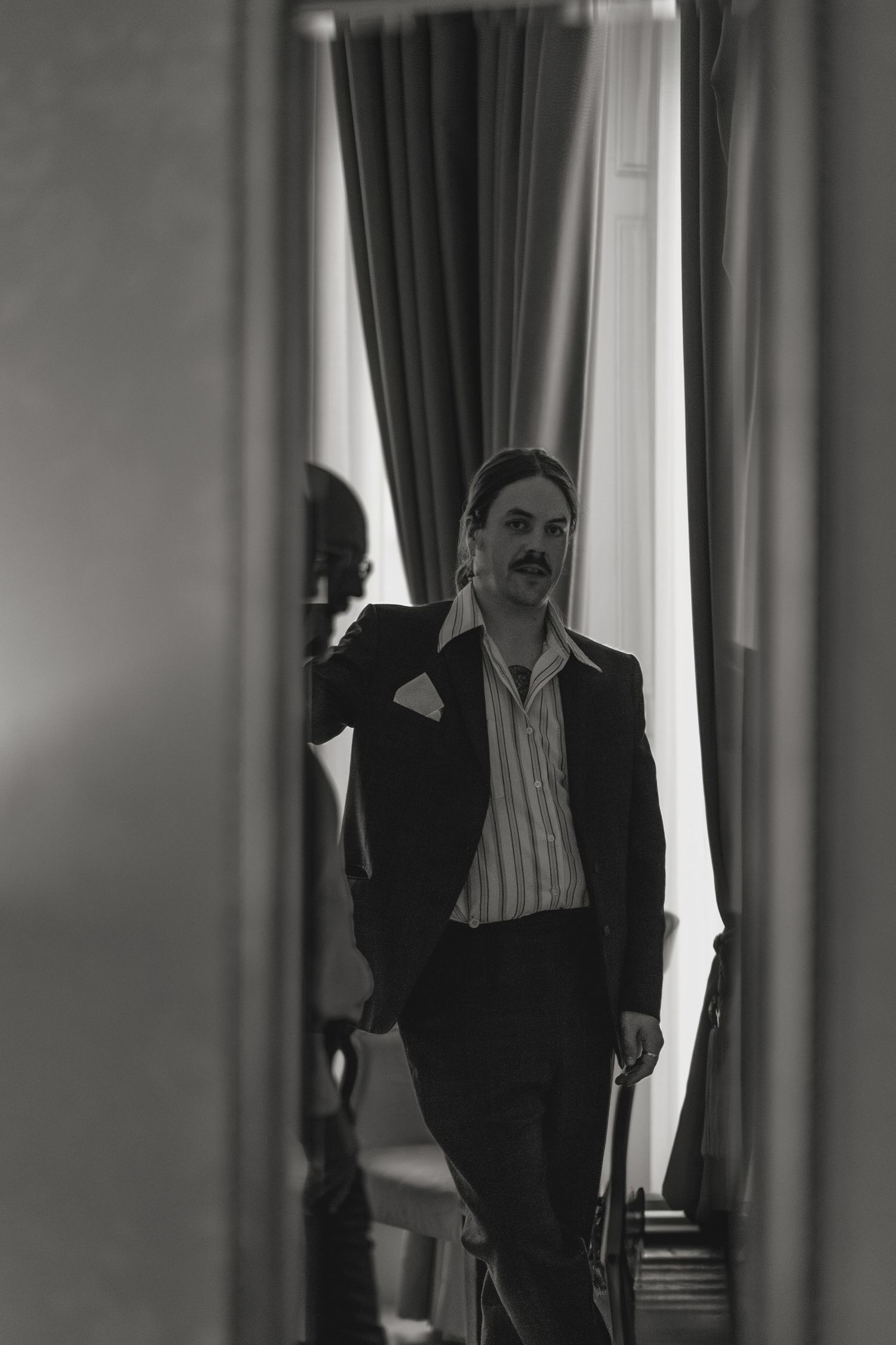 Black and white portrait through doorway of person in formal attire.