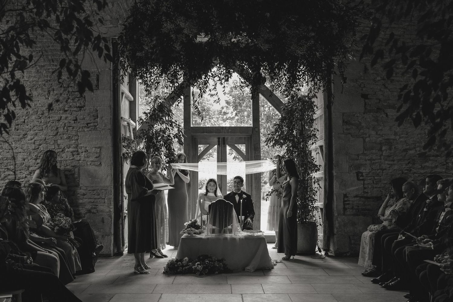 Wedding ceremony silhouettes in a rustic venue with dramatic natural lighting.