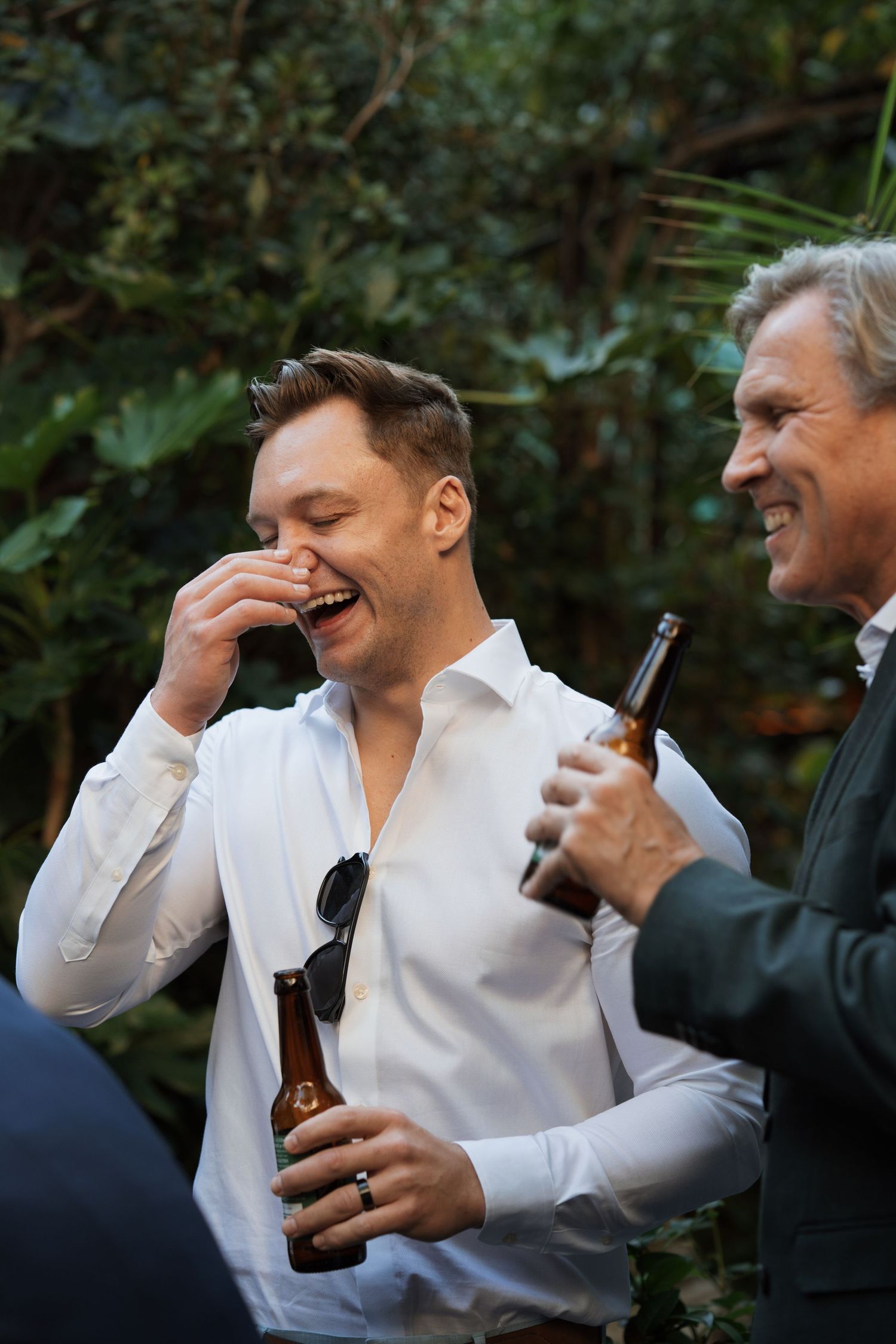 Wedding guest laughing while holding a drink bottle in garden setting.