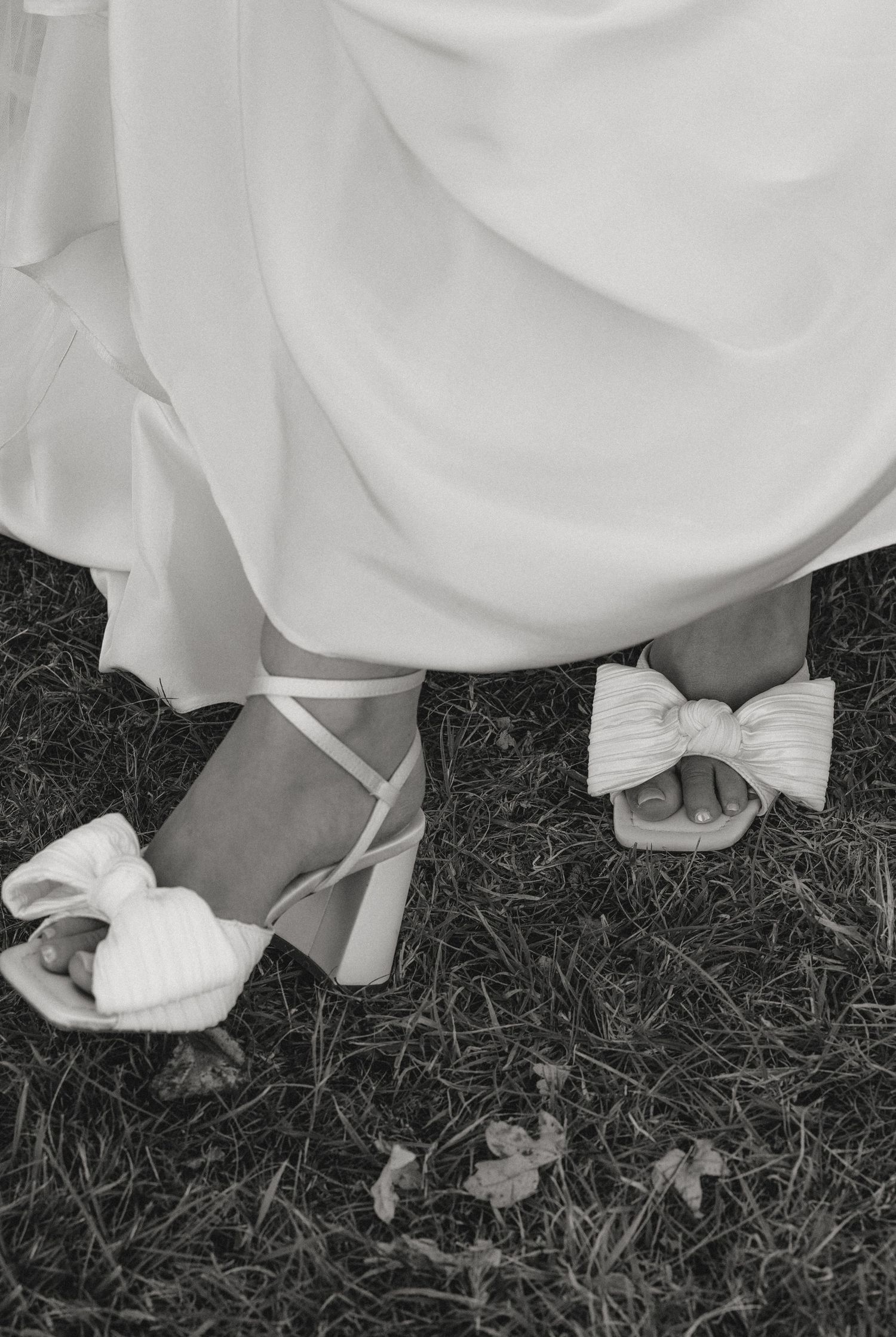 Black and white detail shot of bride's white dress and shoes on grass.