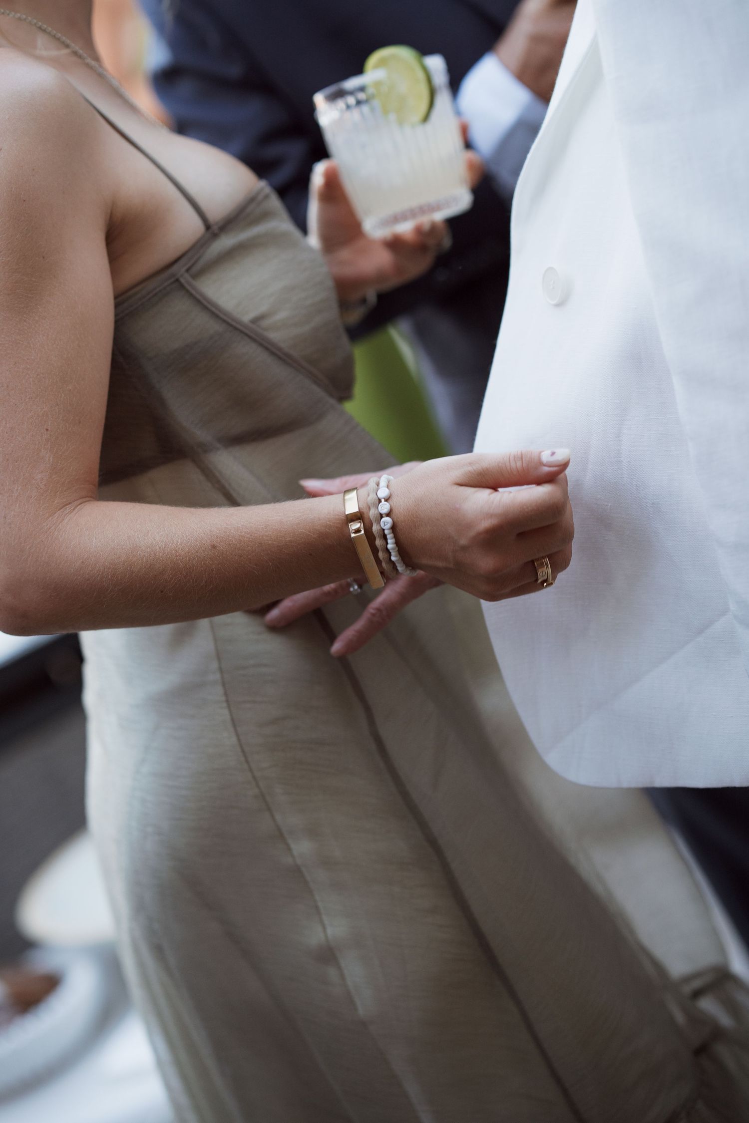 Close-up of hands holding drinks with lime garnishes at an outdoor event.