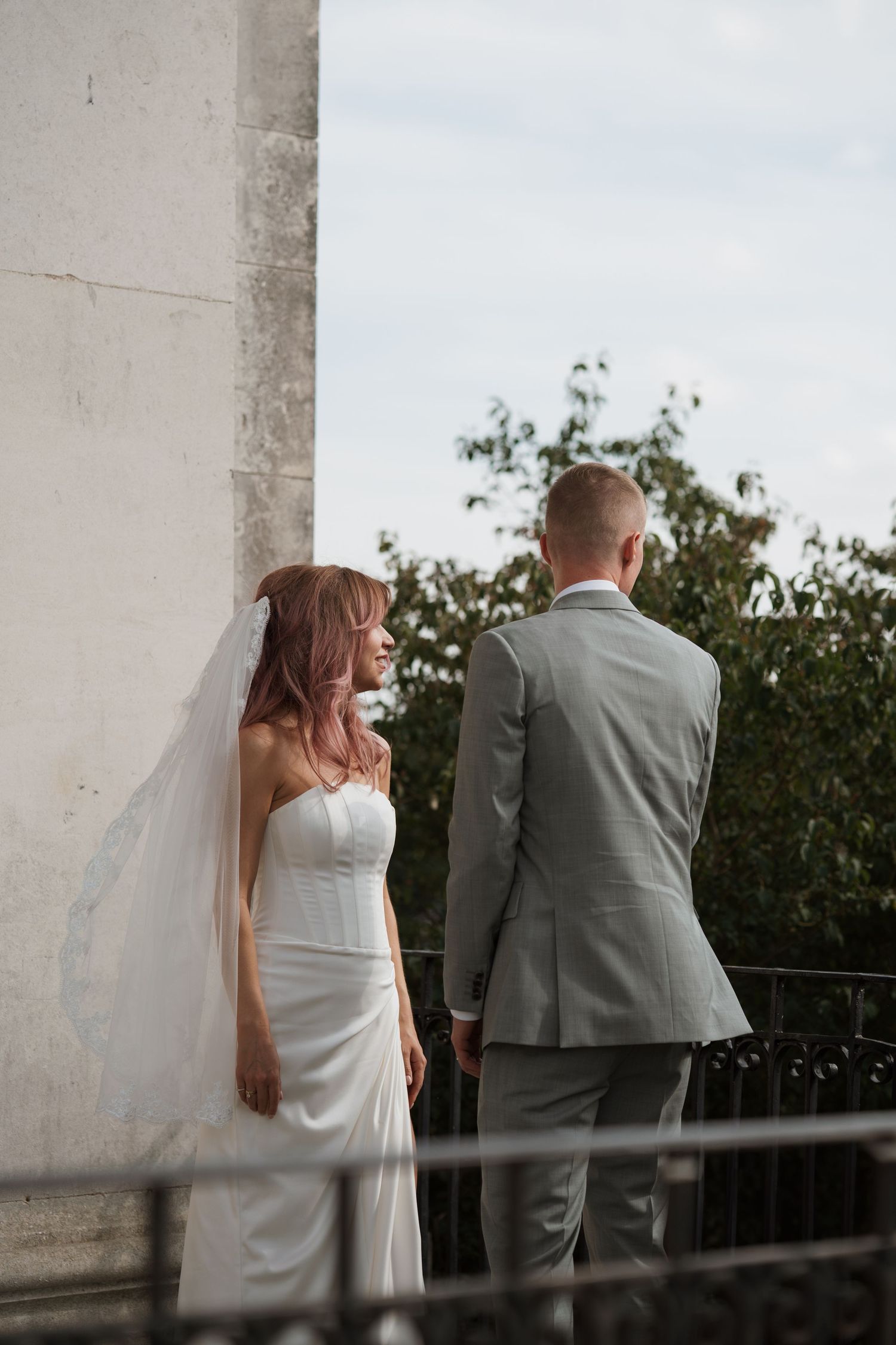 Wedding couple in white dress and grey suit photographed from behind on a balcony.