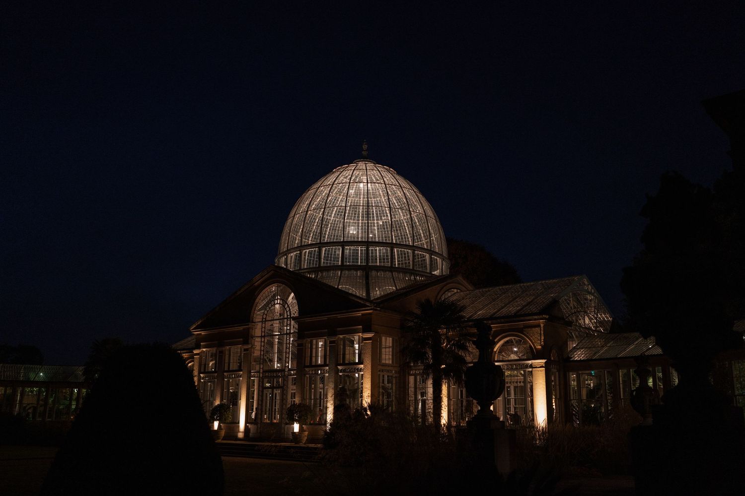 Illuminated glass dome conservatory building at night with architectural lighting.