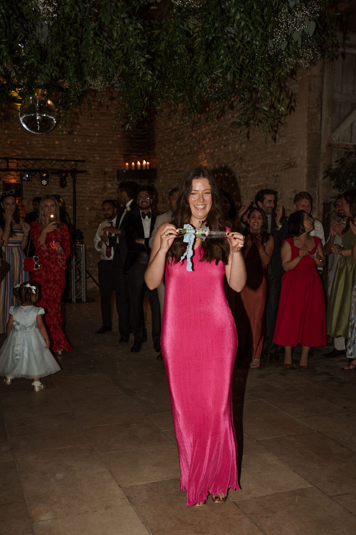 Person in bright pink dress dances joyfully at an indoor celebration.