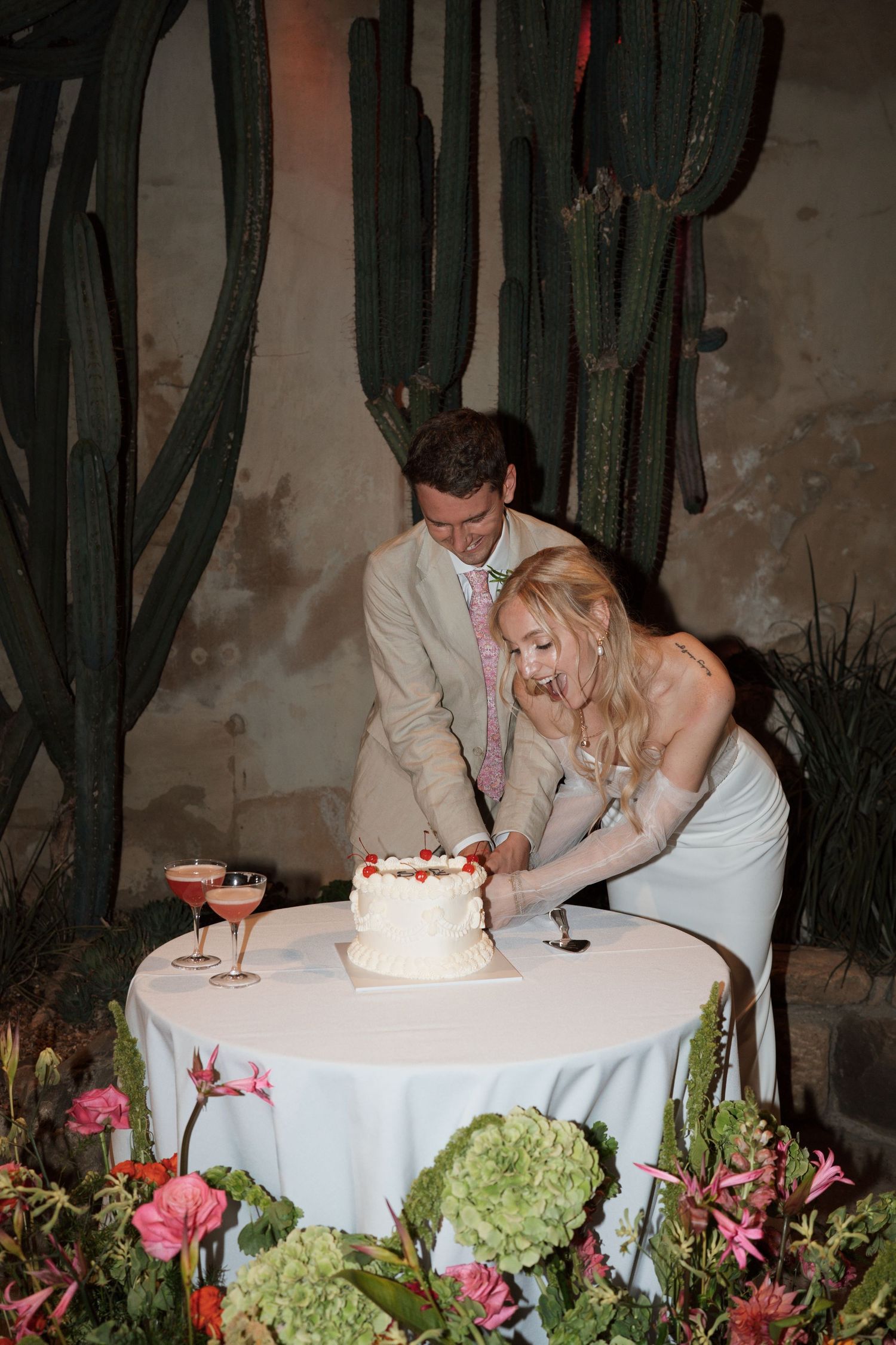 Couple cutting their wedding cake together at a reception surrounded by desert plants and cacti.