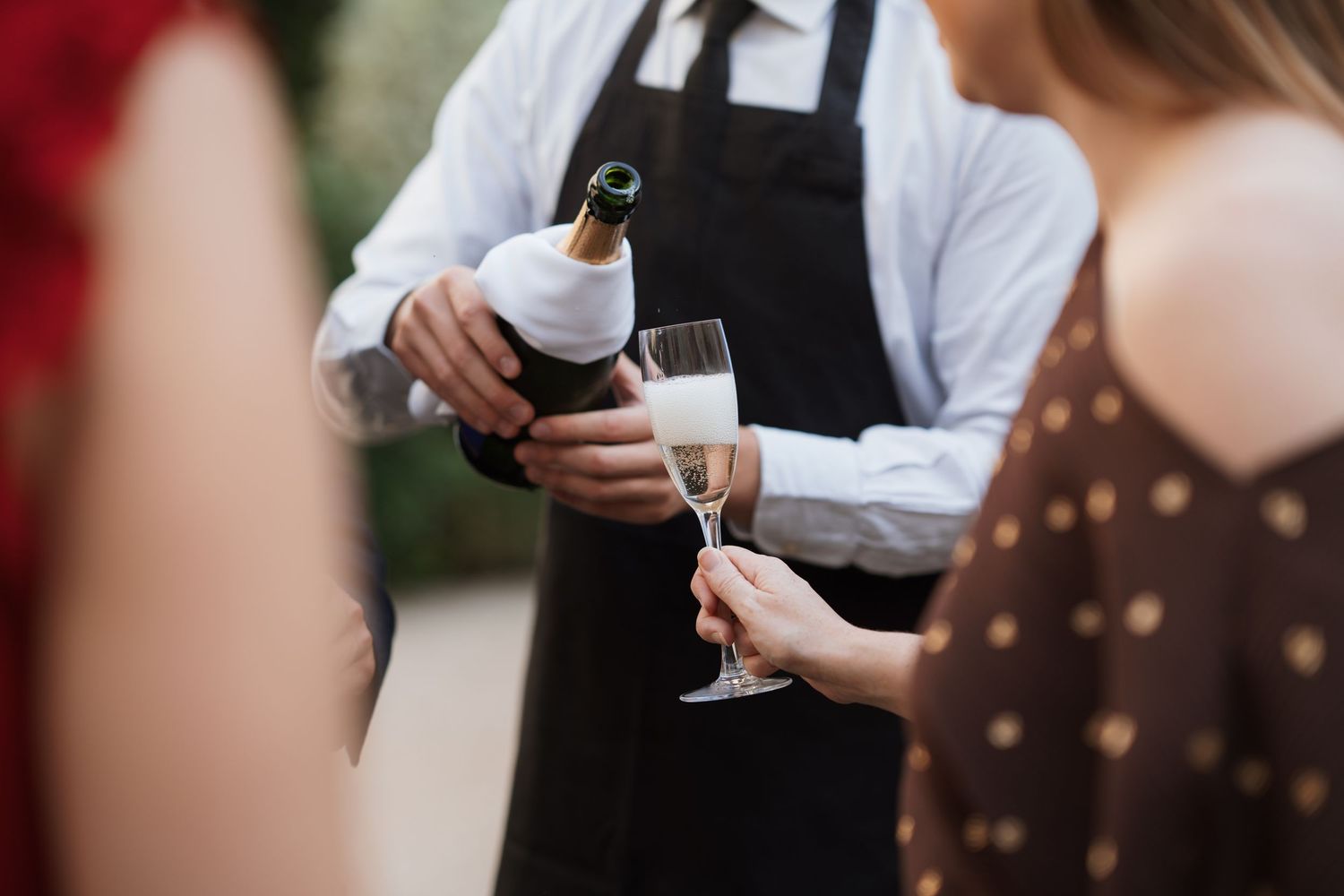 Servers in formal attire carrying drinks on trays at an elegant event.