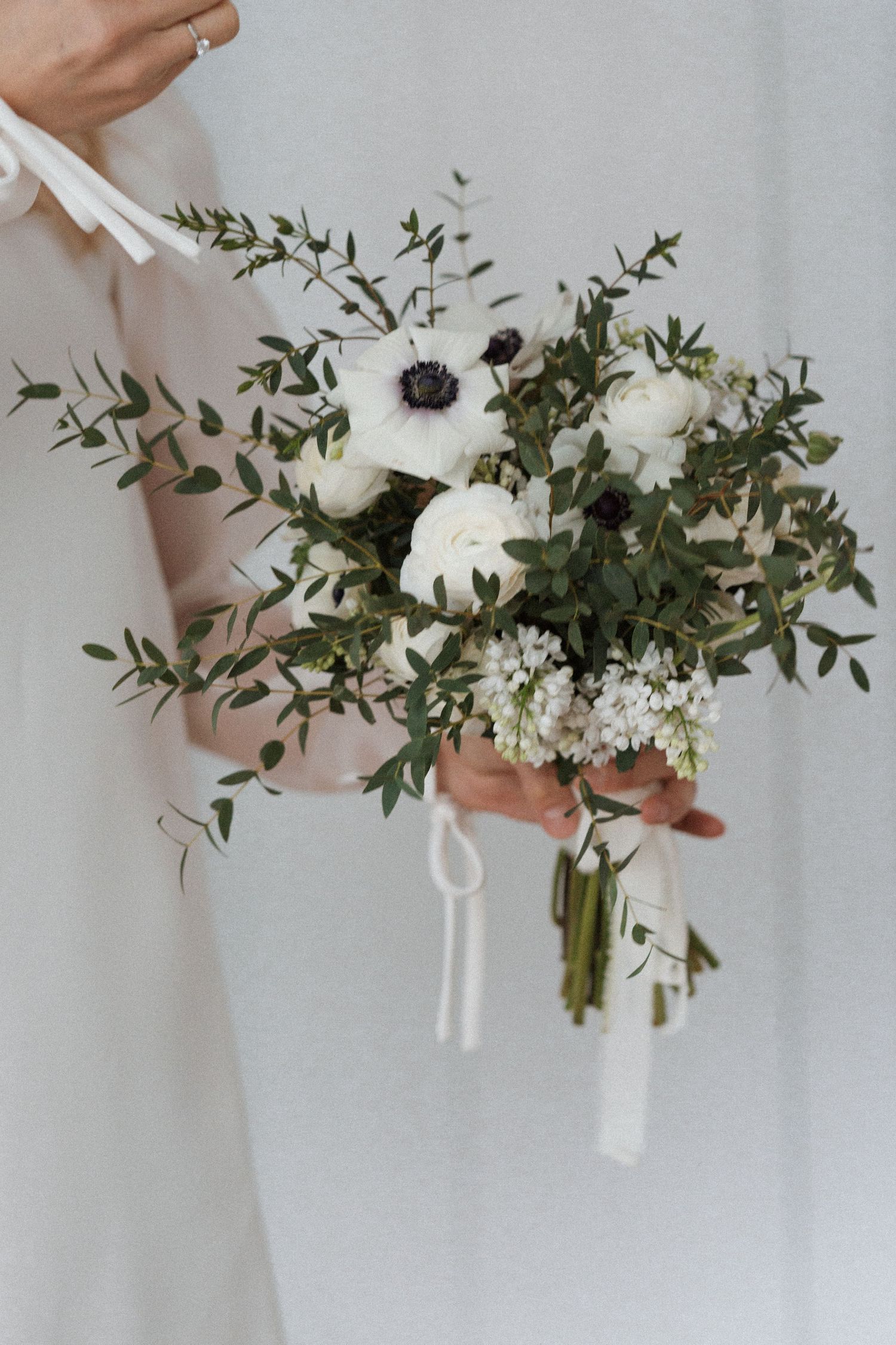 A delicate white floral bouquet with greenery and ribbons being held in natural light.