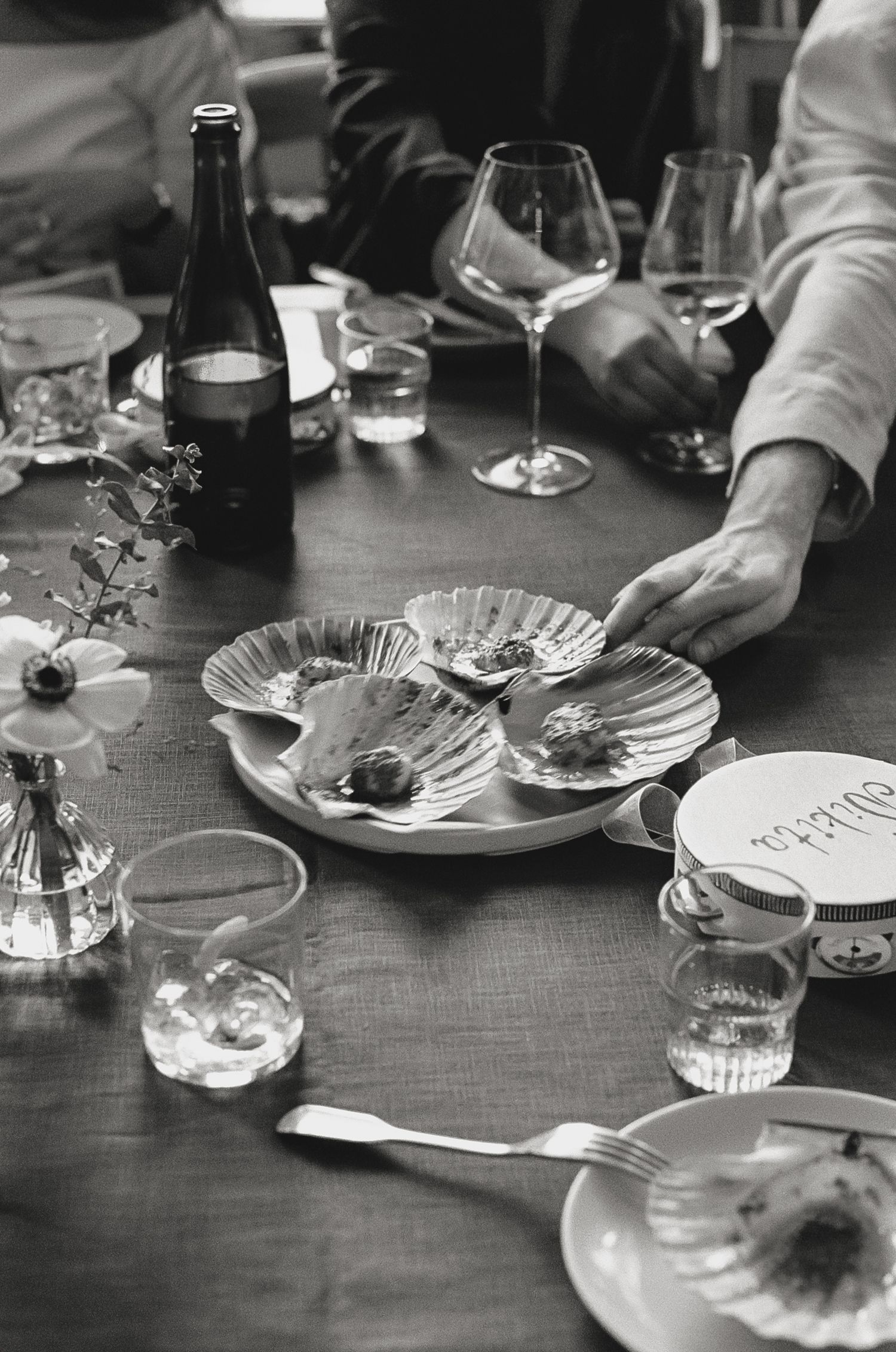 Black and white photo of empty plates and wine glasses on a wooden dining table.