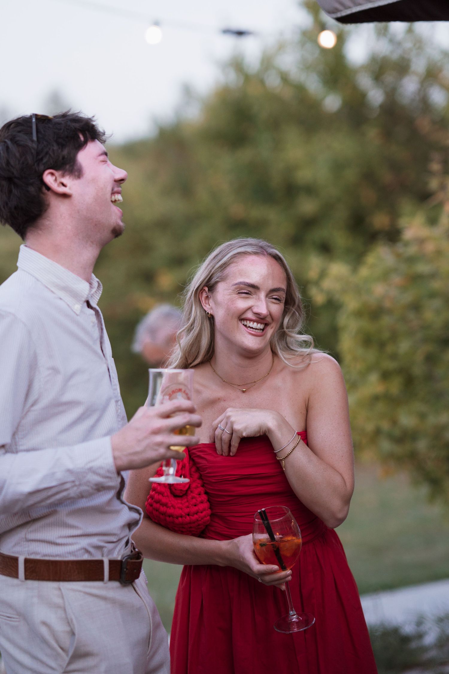 Wedding guests sharing laughter and drinks during an outdoor celebration.