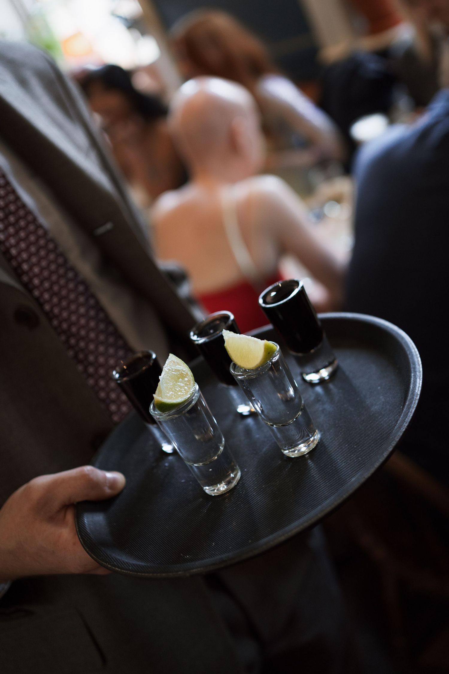 Shot glasses with lemon slices being served on a black tray in a dimly lit setting.