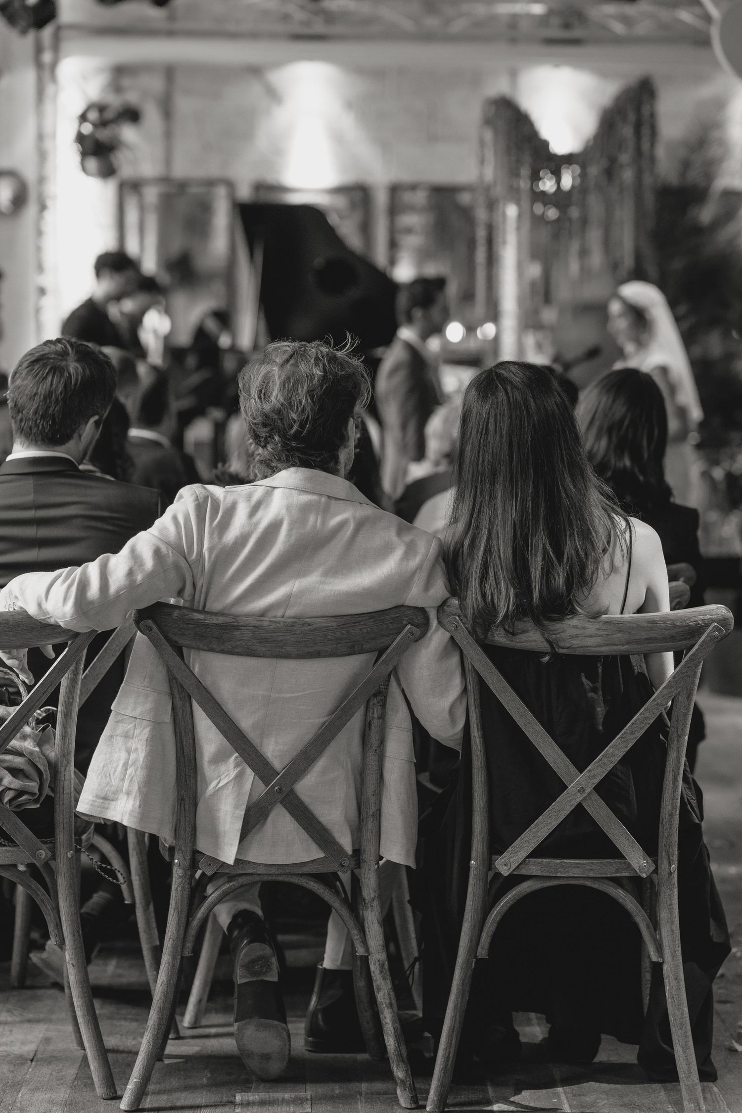 People sitting in wooden chairs at a dimly lit venue seen from behind.