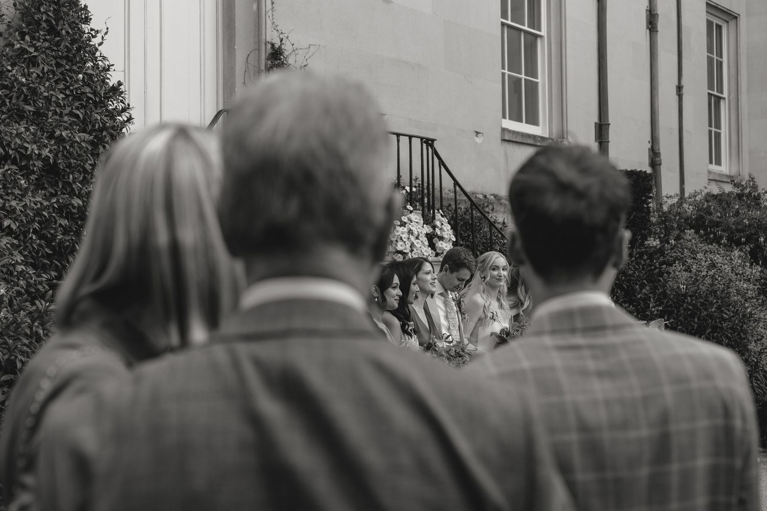 Guests watch a wedding ceremony from behind on the grounds of an elegant estate.