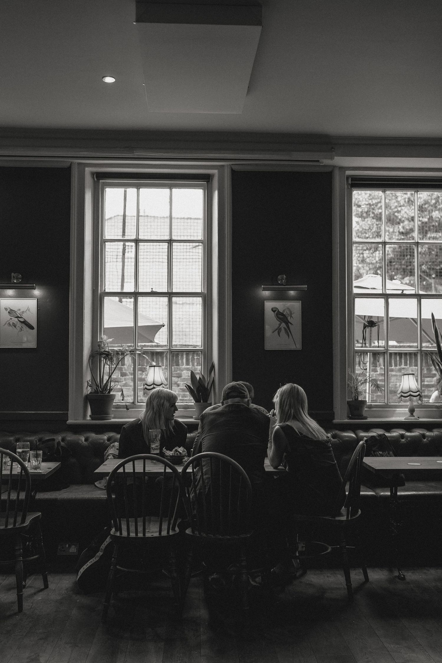 Interior of a dark restaurant dining room with large windows letting in natural light.
