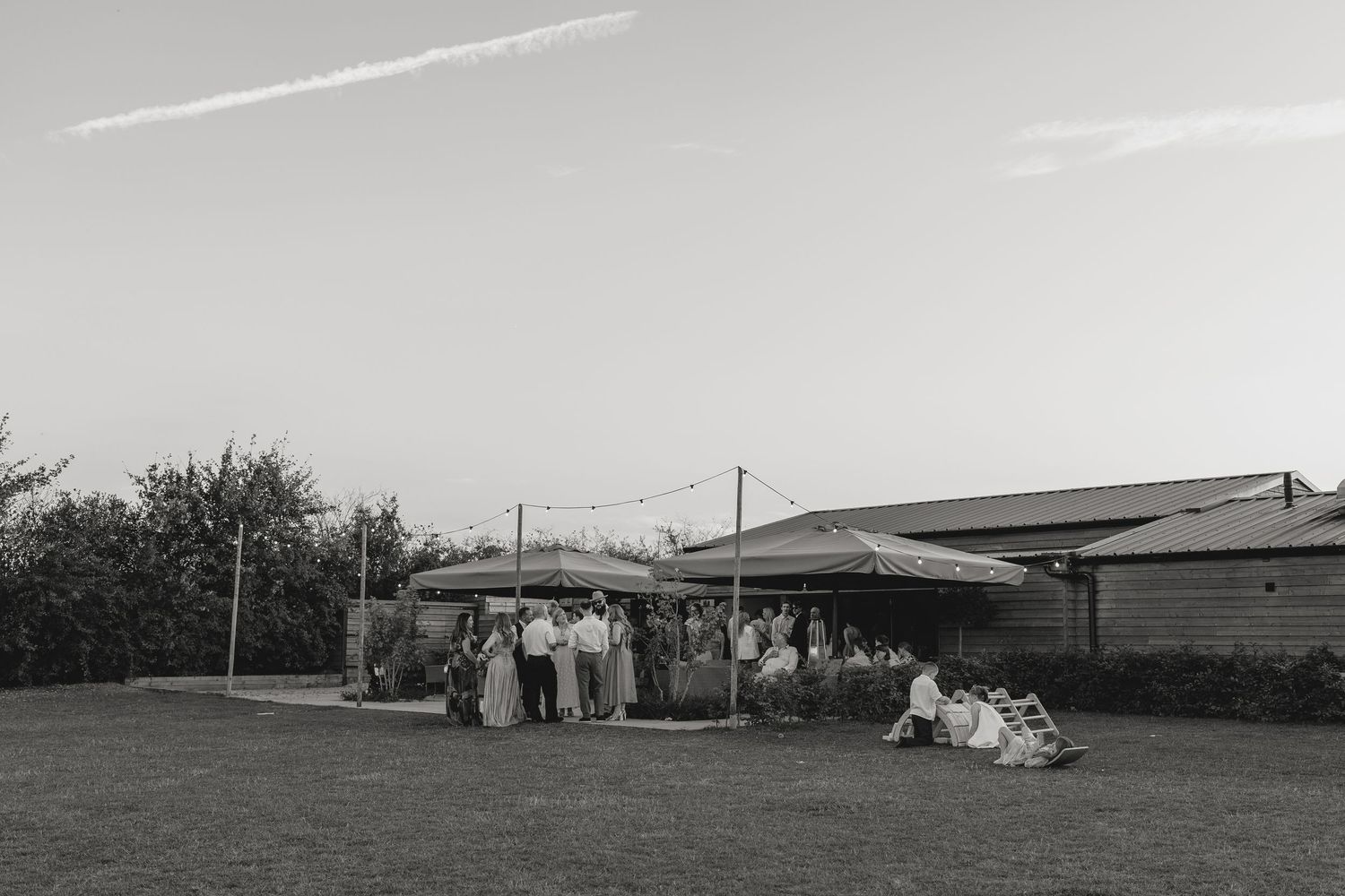 Black and white photo of wedding guests gathered outside on a lawn.