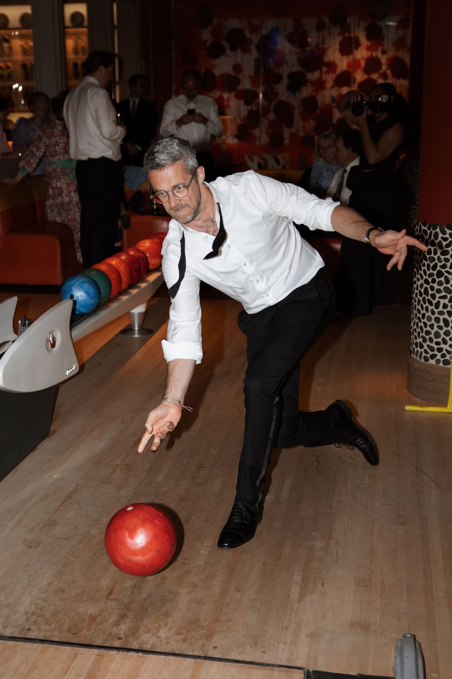 Person in formal attire bowling at an indoor bowling alley during what appears to be a special event.
