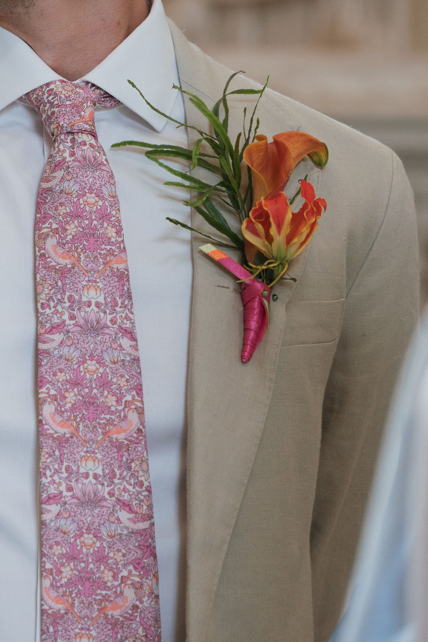 A pink floral tie and orange boutonniere accent a light beige suit jacket.