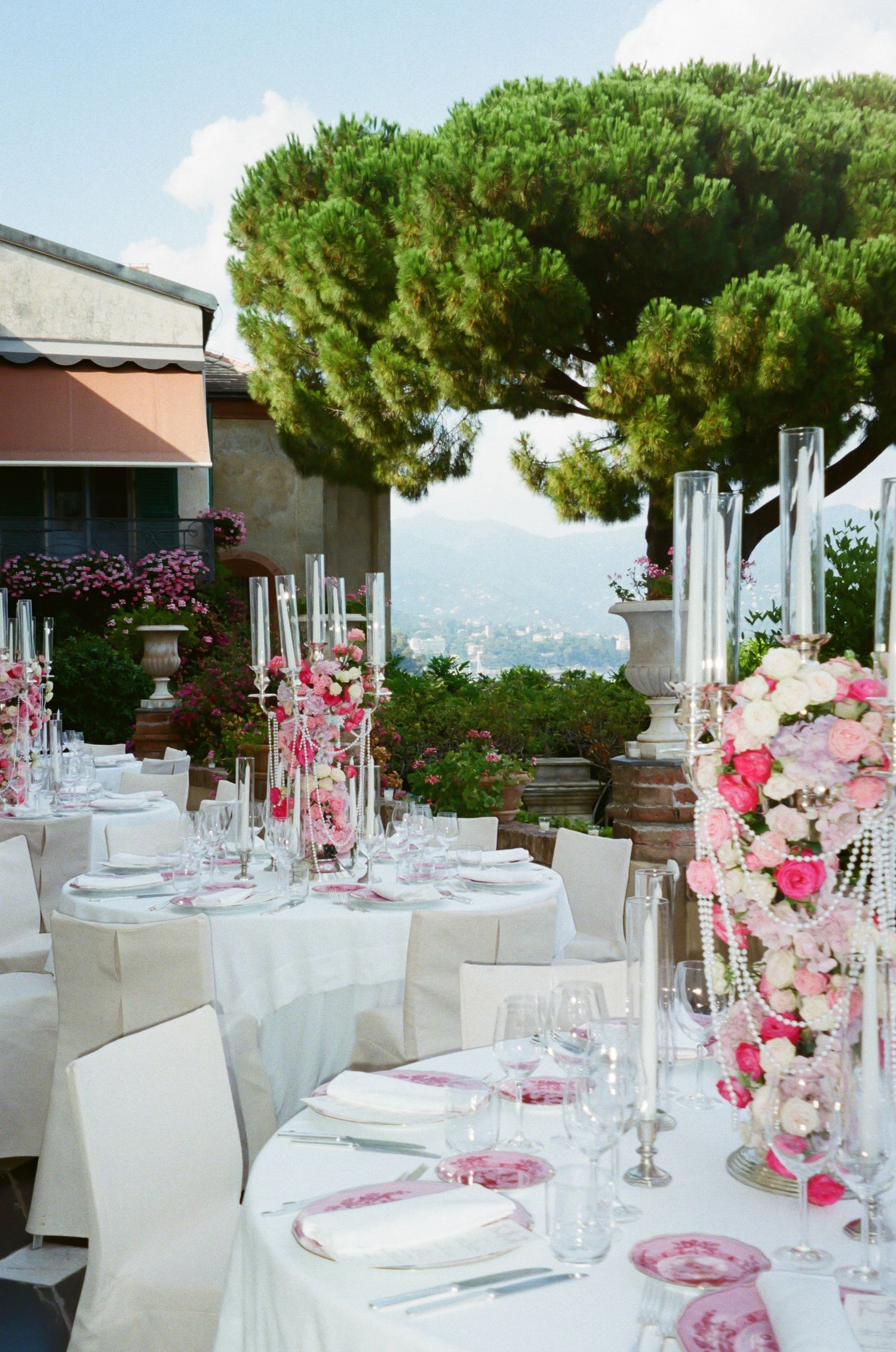 Outdoor wedding reception tables decorated in white and pink with Mediterranean views.