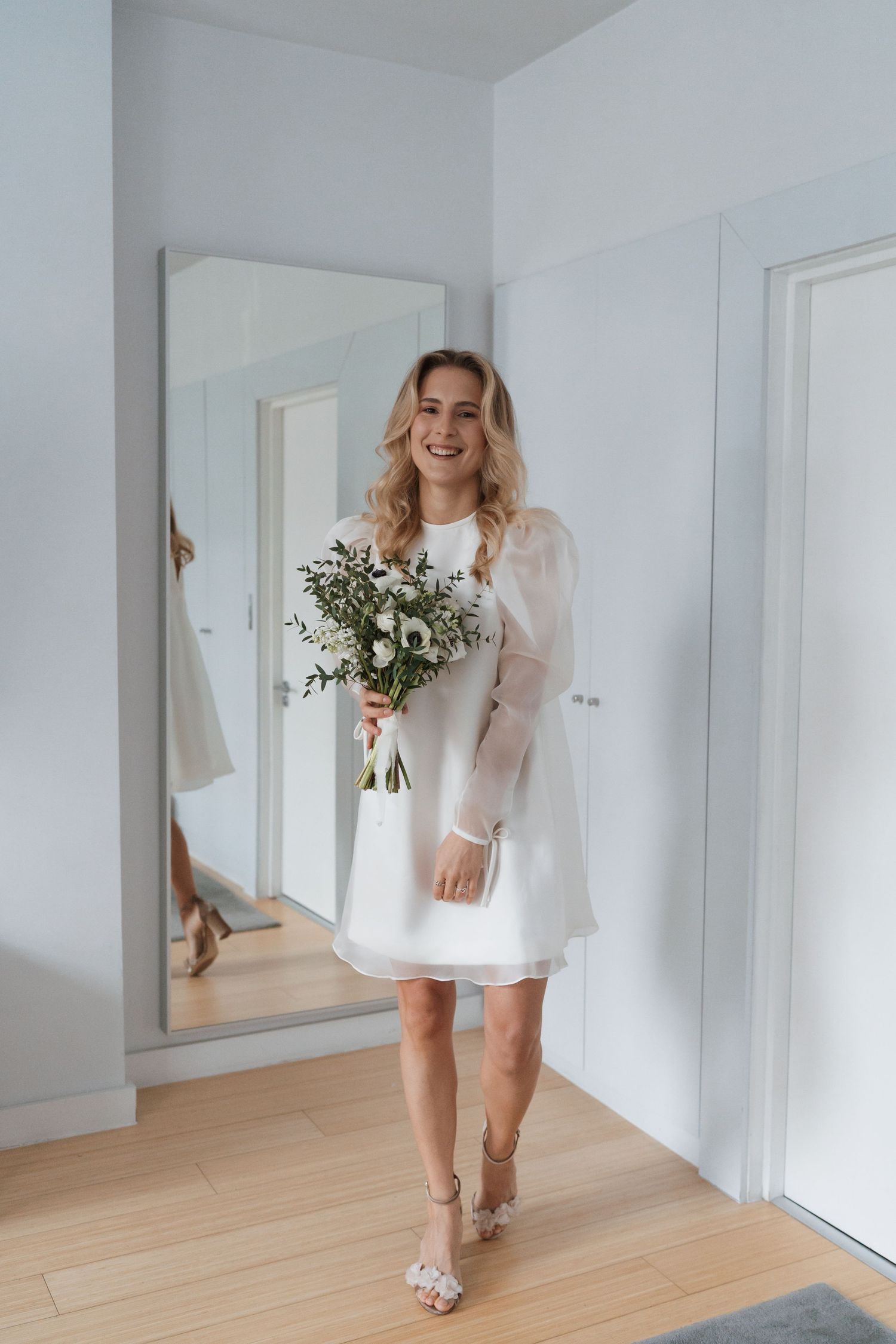 Someone in a white mini dress walking through a bright modern interior space with wooden floors.