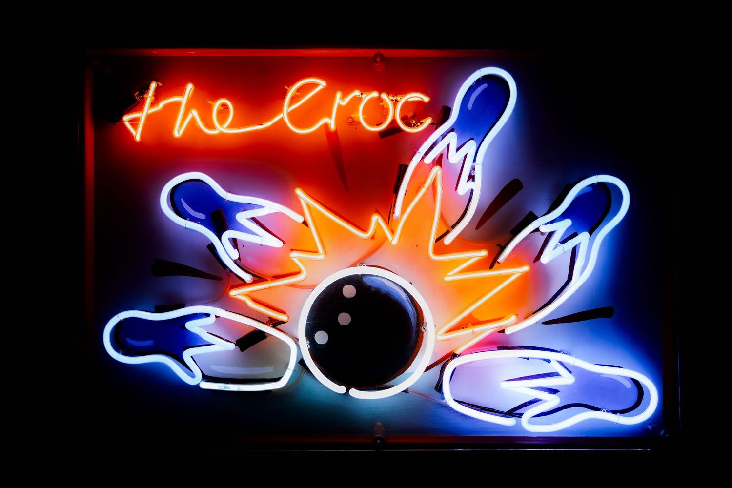 Neon blue and orange sign for 'The Croc' illuminated in the dark.