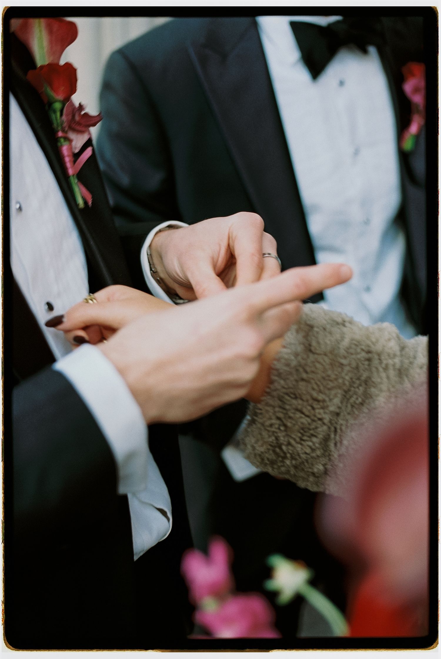 Close-up of hands exchanging wedding rings during a formal ceremony with flowers in the background.