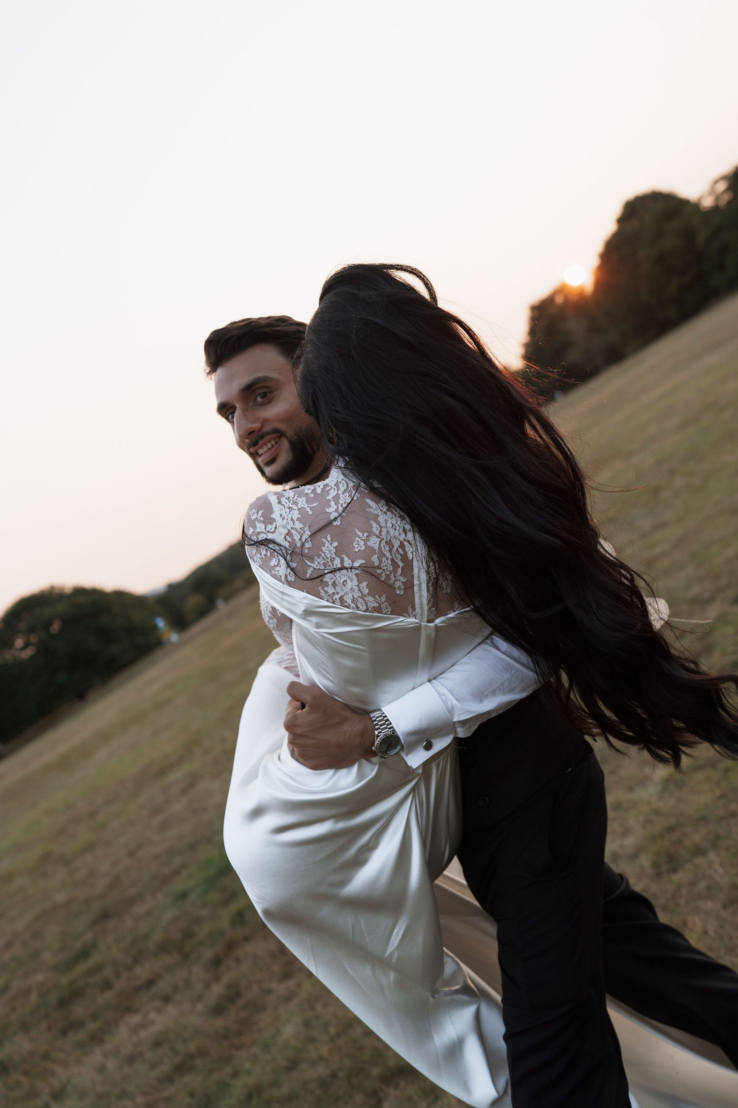 A couple embraces in a spinning dance move at sunset in a grassy field.