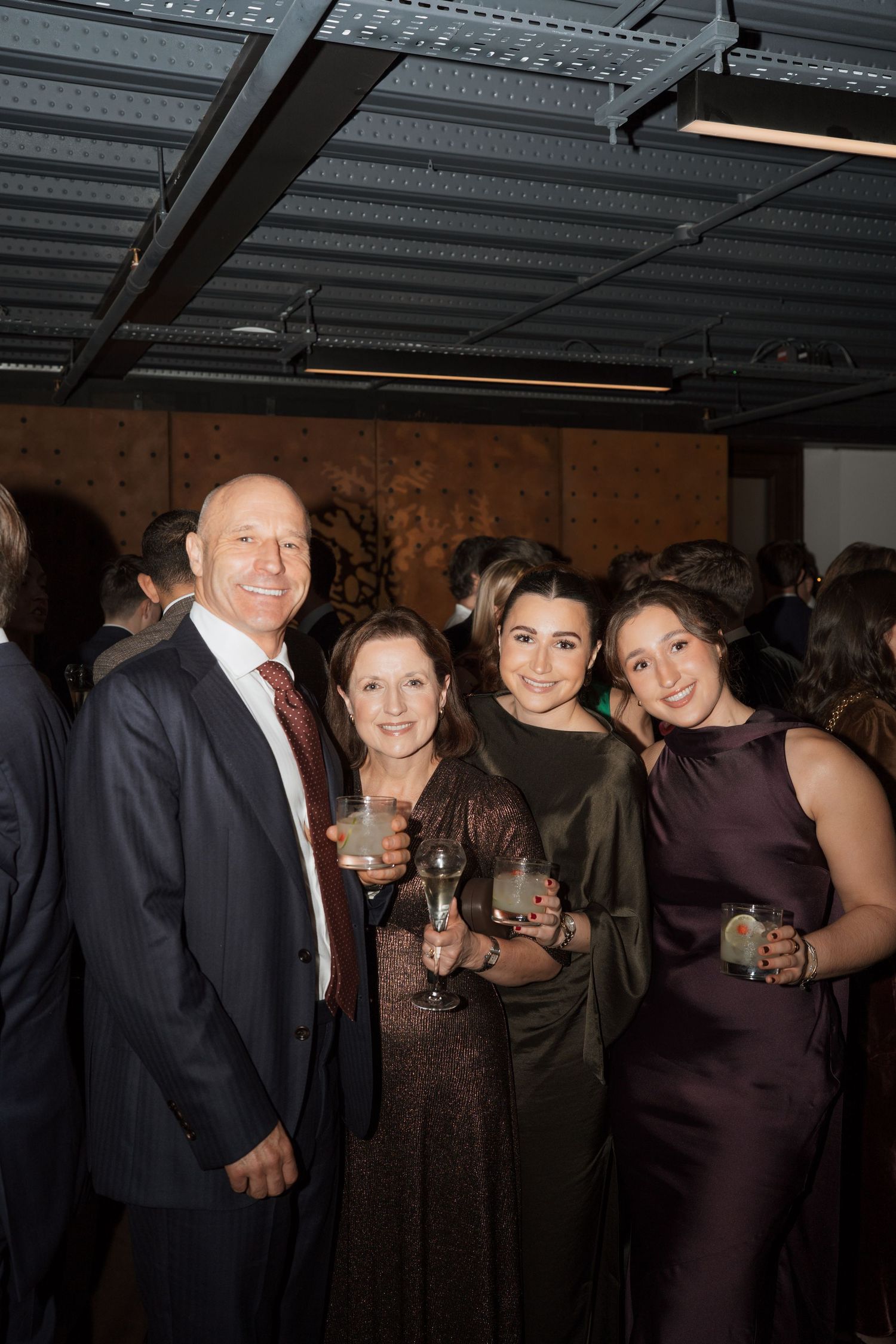 Guests in formal attire socializing at an indoor event with industrial ceiling.