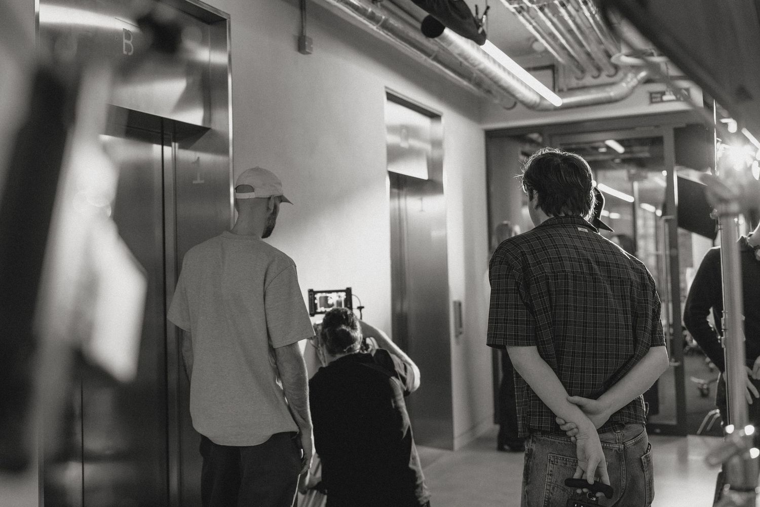 Black and white photo of a film crew shooting near elevators in an indoor location.