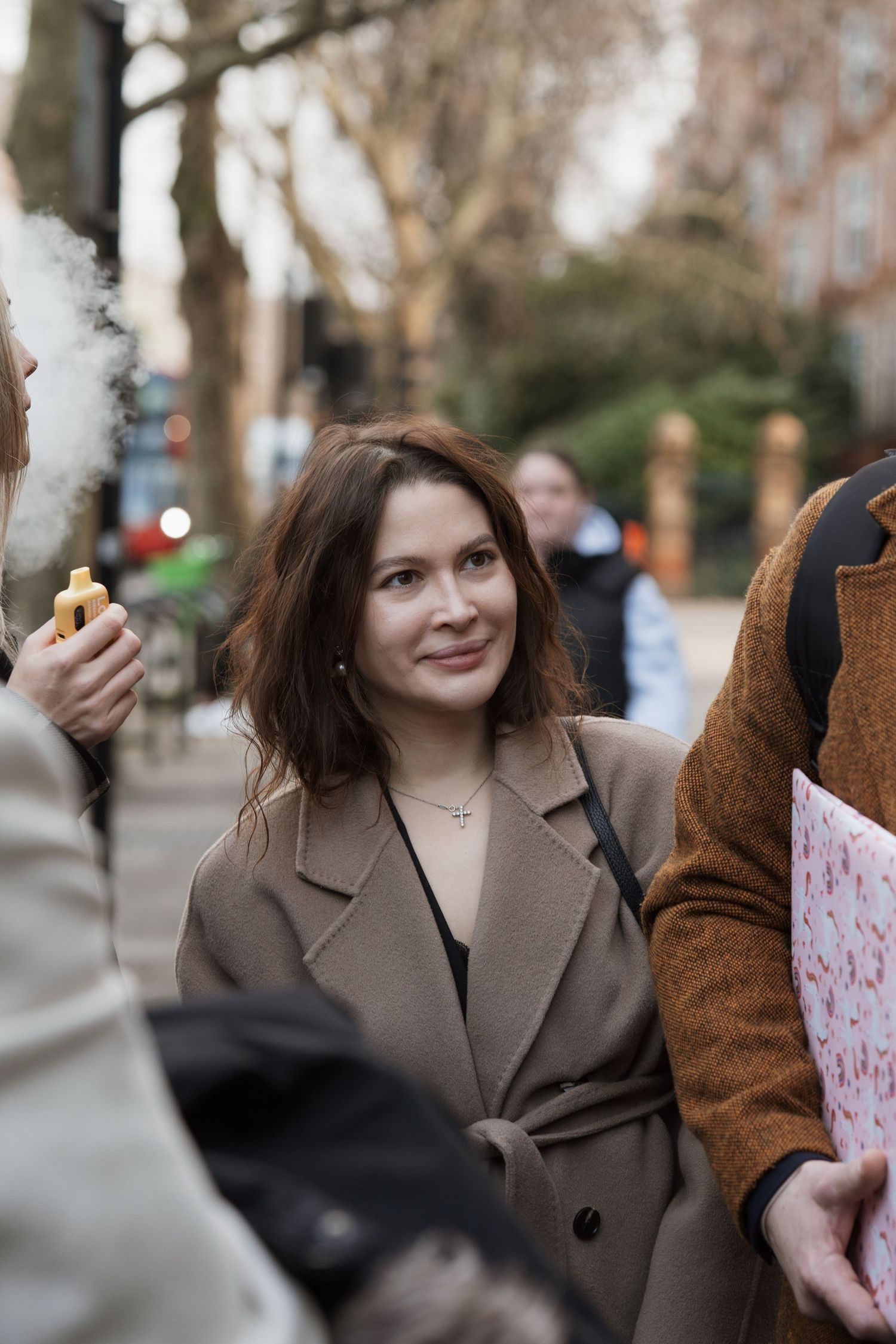 Person in a brown coat walking outdoors on a winter day carrying papers.