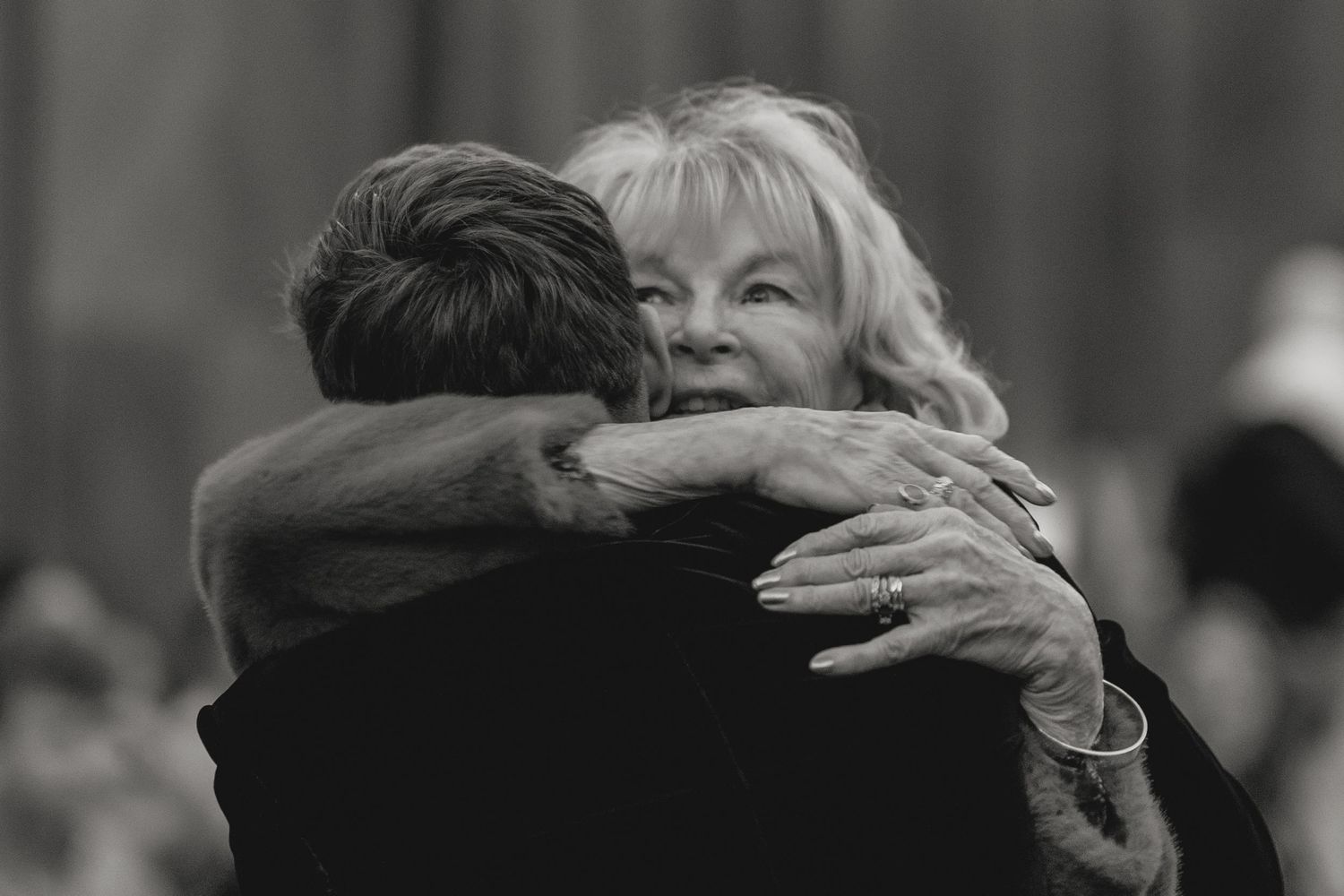 Two people sharing a warm embrace at a formal gathering.