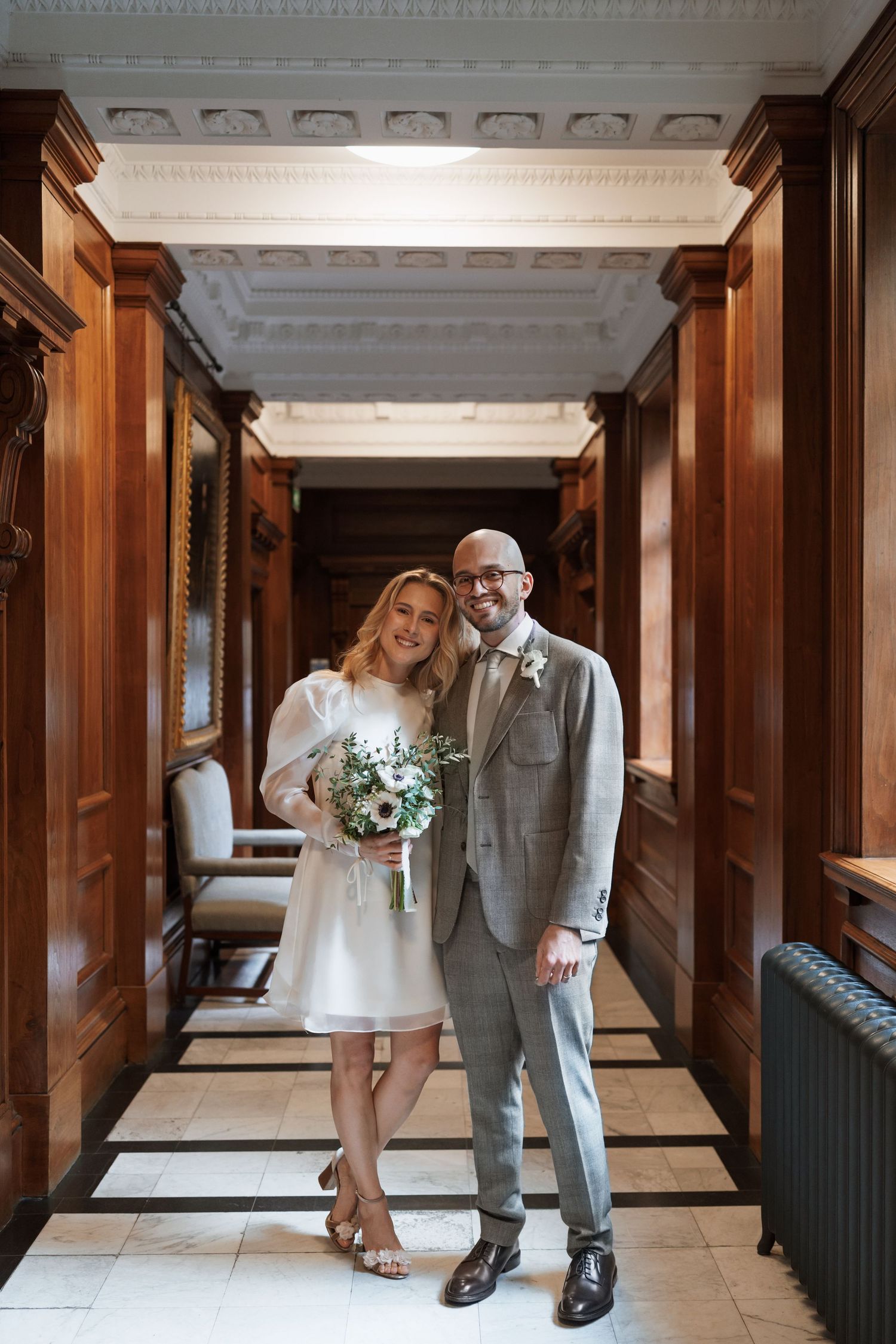 Elegant couple walking through wood-paneled hallway with ornate ceiling details.